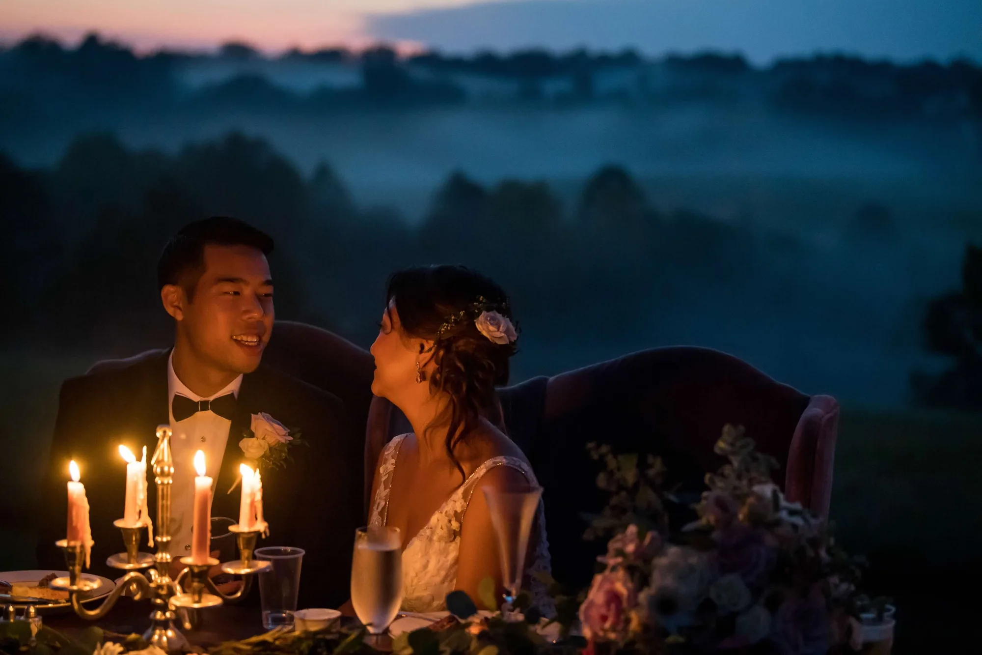 Bride and groom share a candlelit twilight moment at sweetheart table overlooking misty Virginia countryside