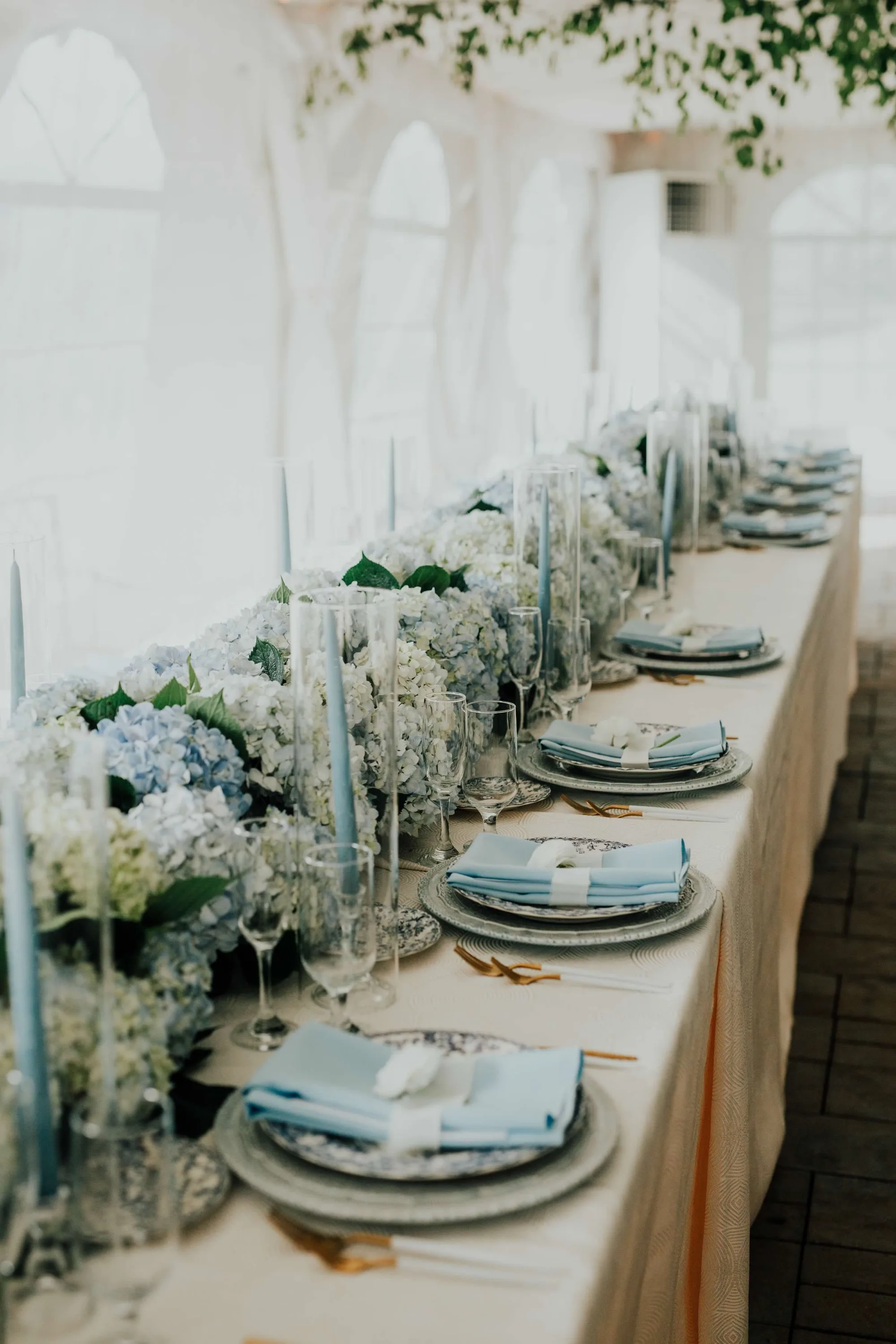 Elegant reception tablescape with blue hydrangeas, taper candles, and blue linen napkins under Rixey Manor's white tent