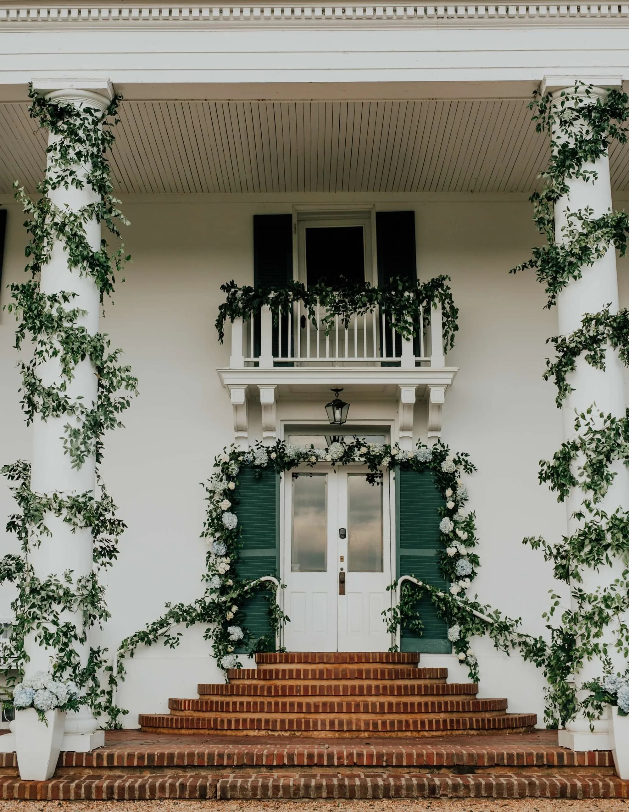 Rixey Manor front entrance adorned with white hydrangeas and lush greenery climbing white columns