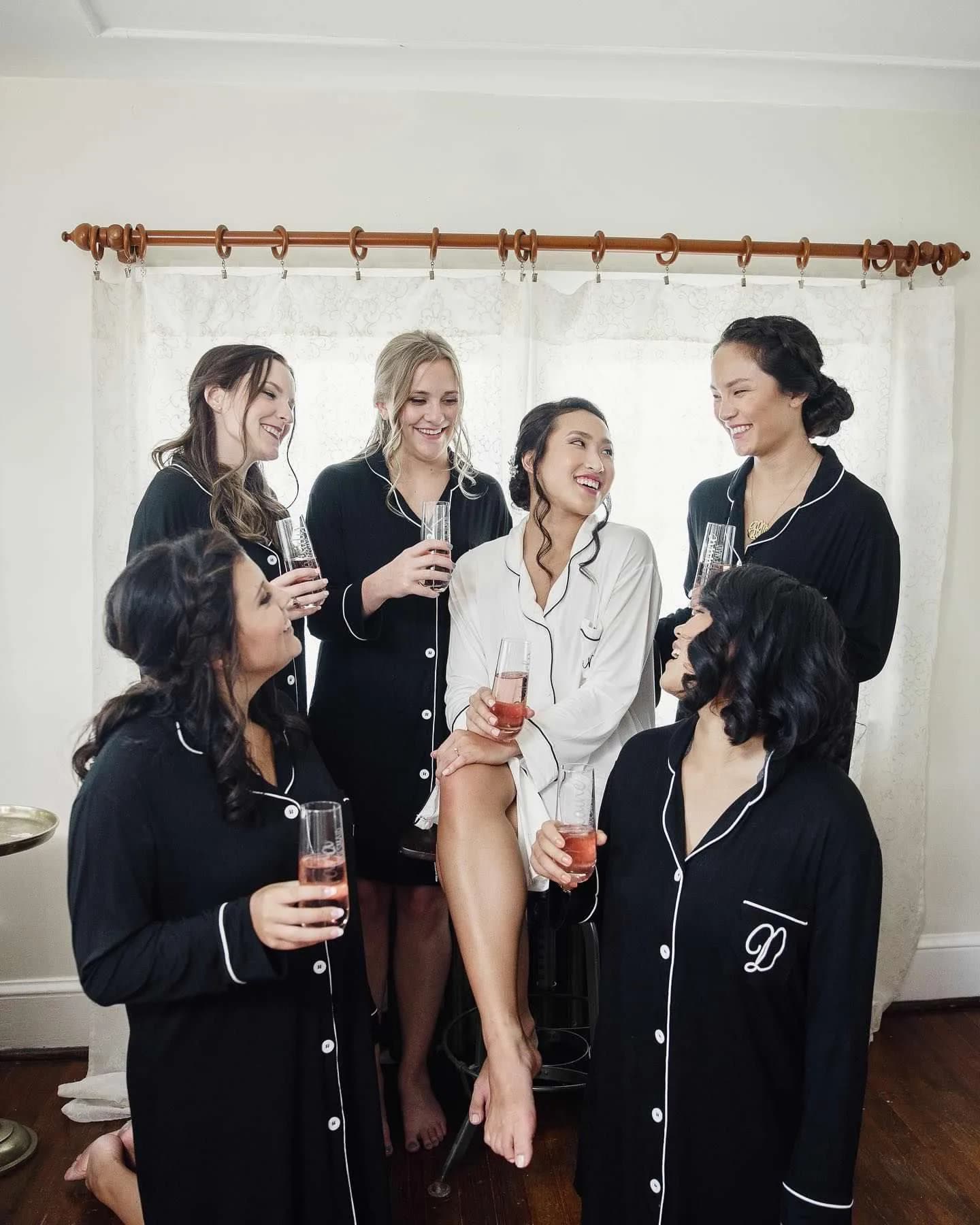 Six women in black pajamas with wine glasses in a bridal getting-ready photo indoors