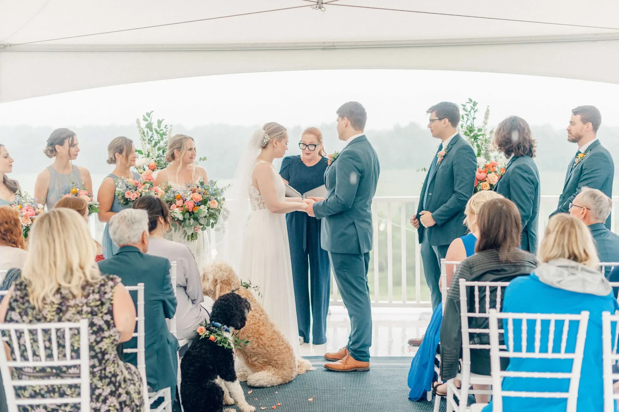 Bride and groom exchange vows under Rixey Manor's terrace tent with flower-crowned dogs seated nearby
