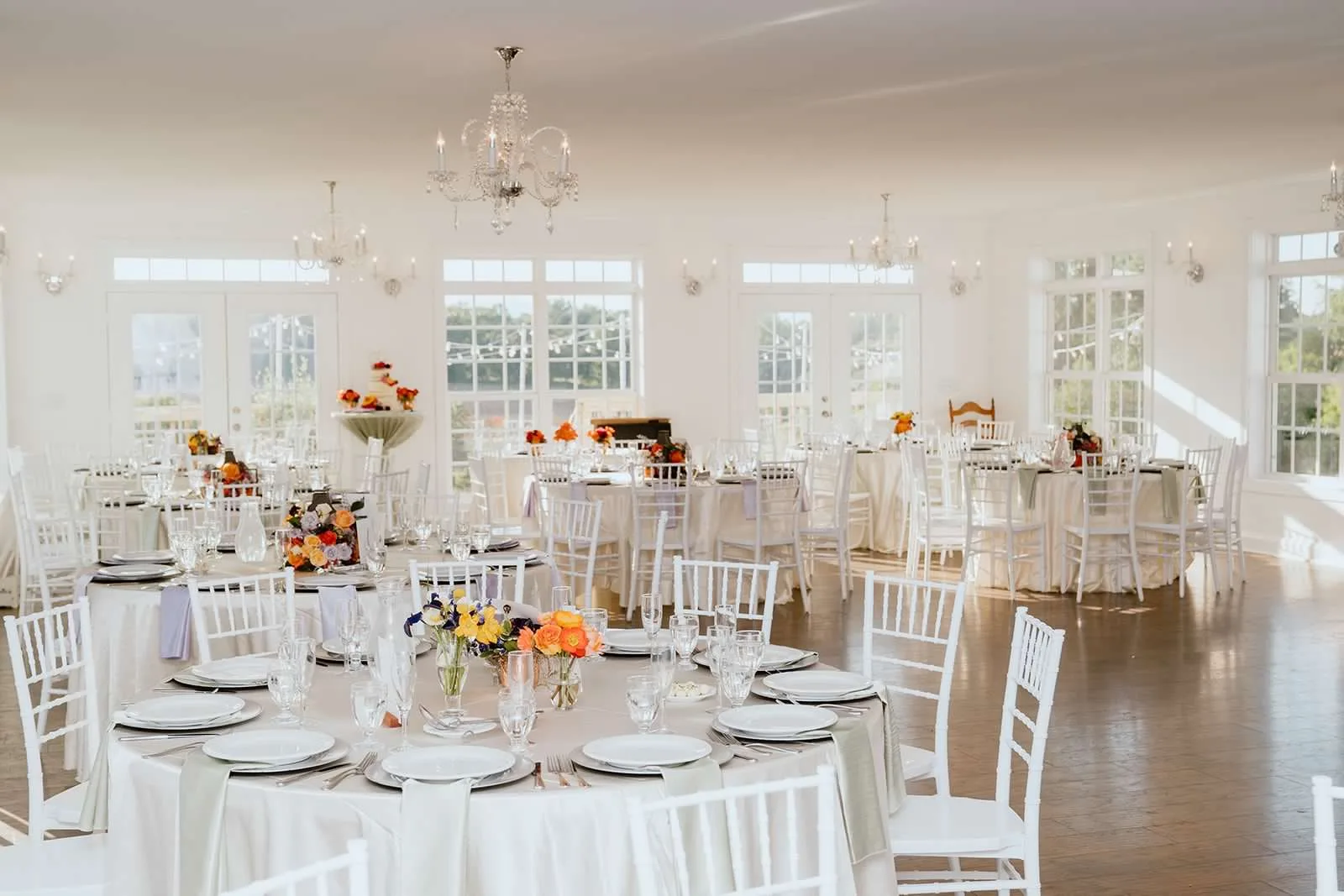 Bright white reception ballroom at Rixey Manor with round tables, chiavari chairs, and colorful floral centerpieces