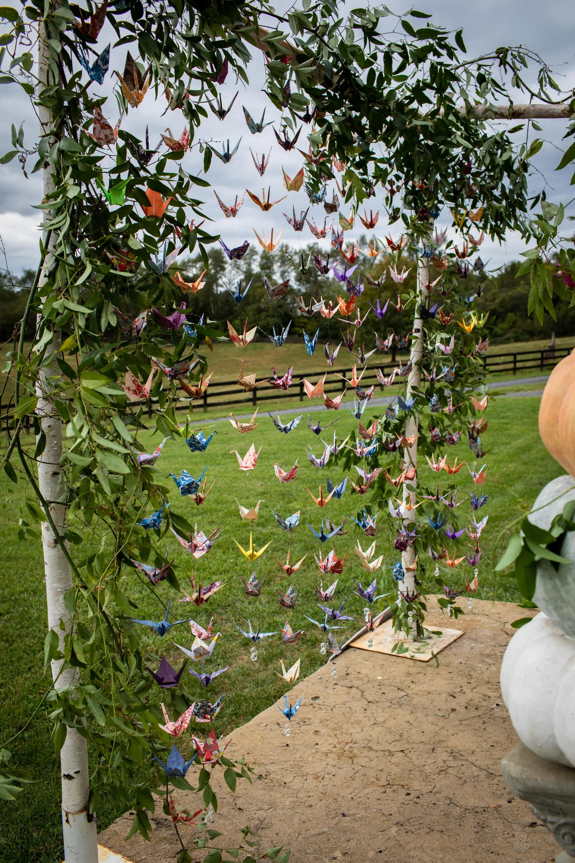 Colorful origami crane curtain hanging from a birch arch draped in greenery at Rixey Manor outdoor ceremony site