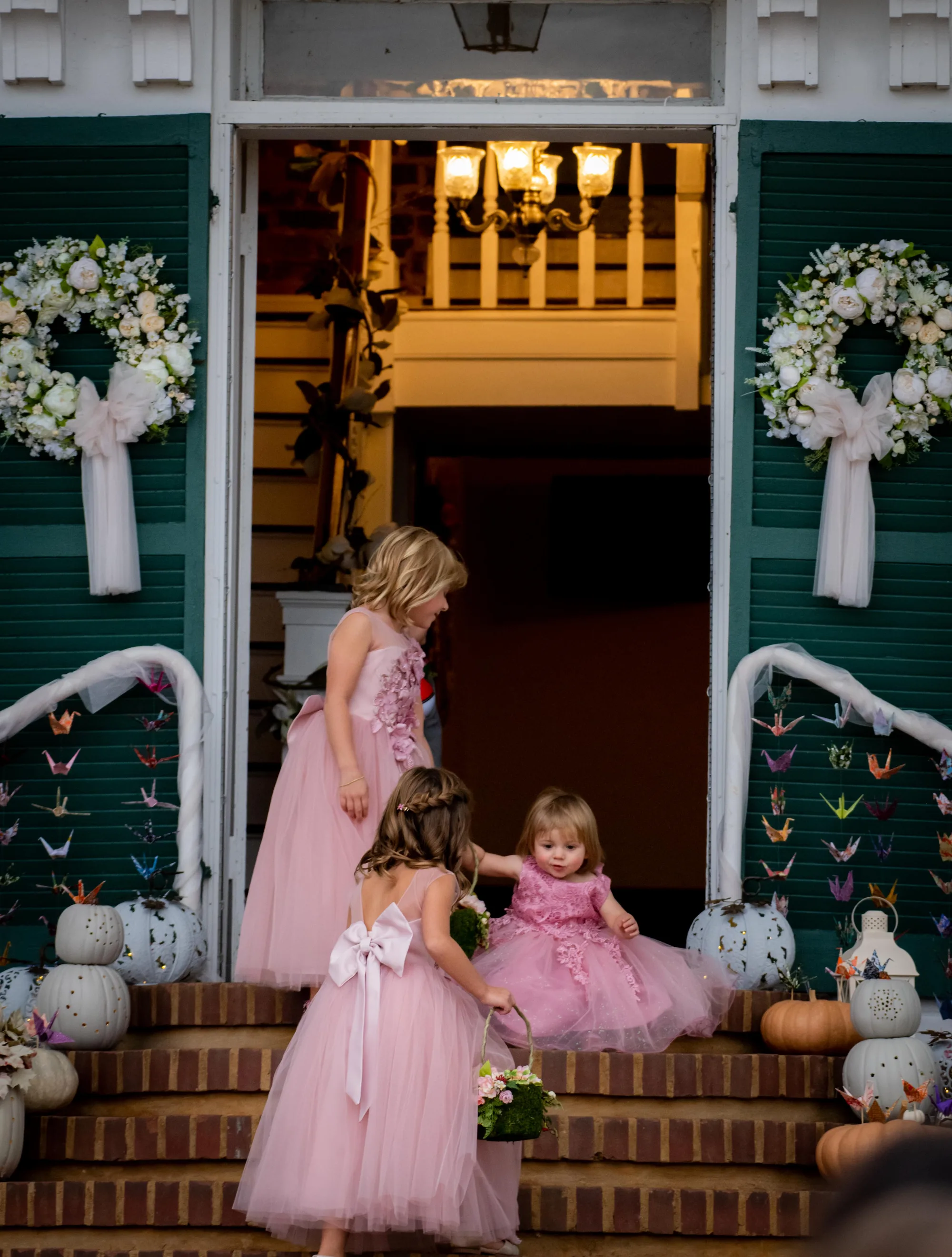Three flower girls in pink dresses climbing brick steps at Rixey Manor's floral-decorated entrance at dusk