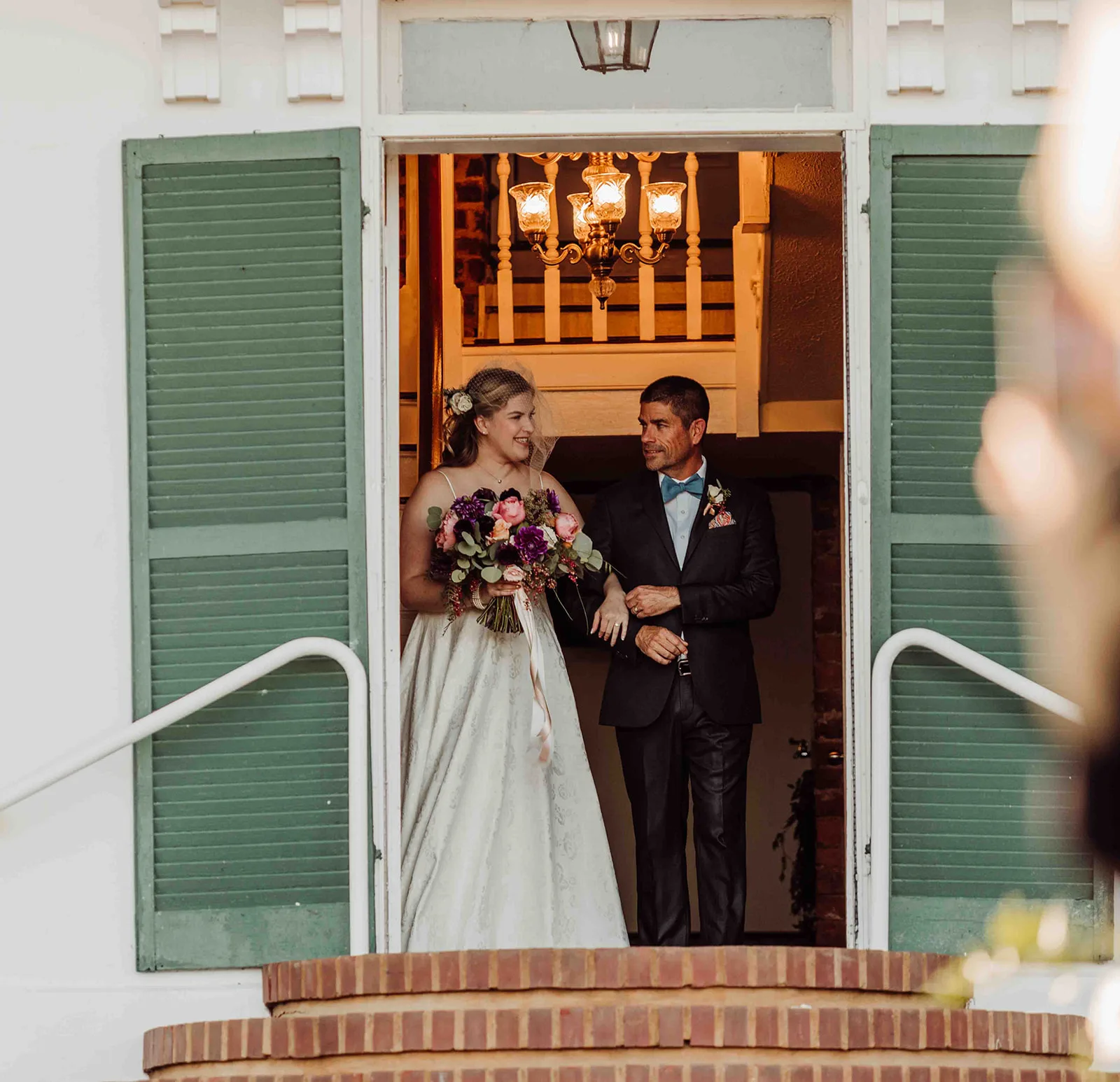 Bride and escort emerge smiling through Rixey Manor's shuttered double doors onto the brick entry steps
