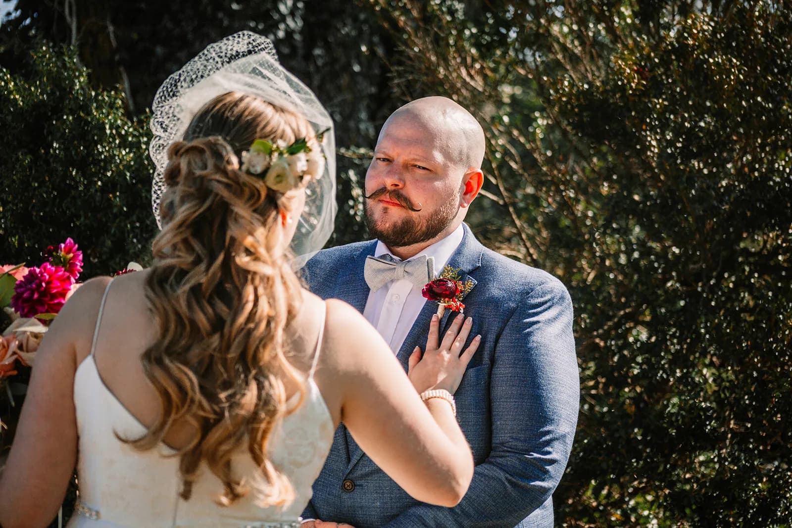 Groom with mustache and boutonniere gazes emotionally at bride during outdoor wedding ceremony vows