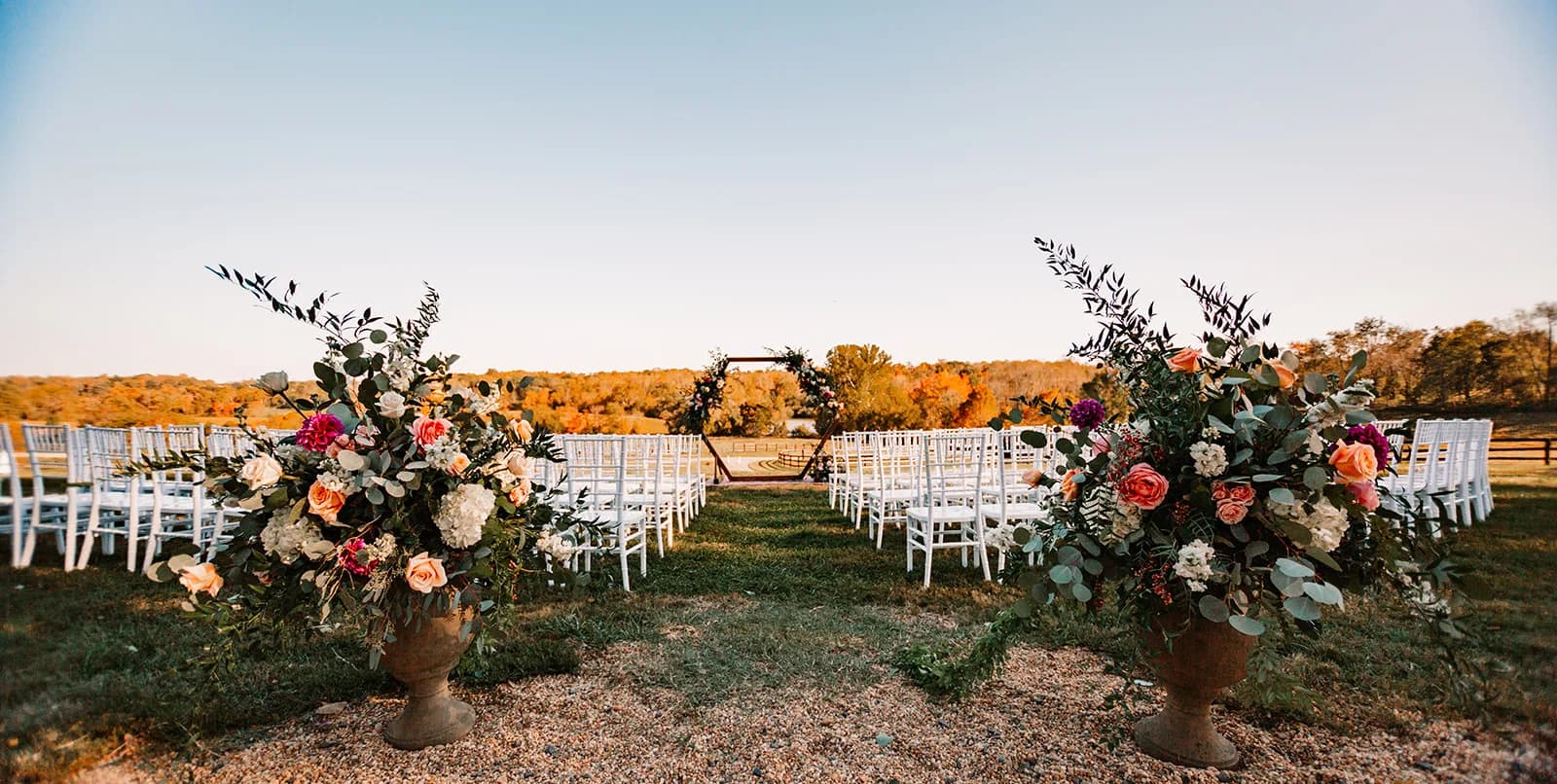 Outdoor ceremony aisle flanked by lush floral urns leading to hexagonal arch at golden hour in rural Virginia