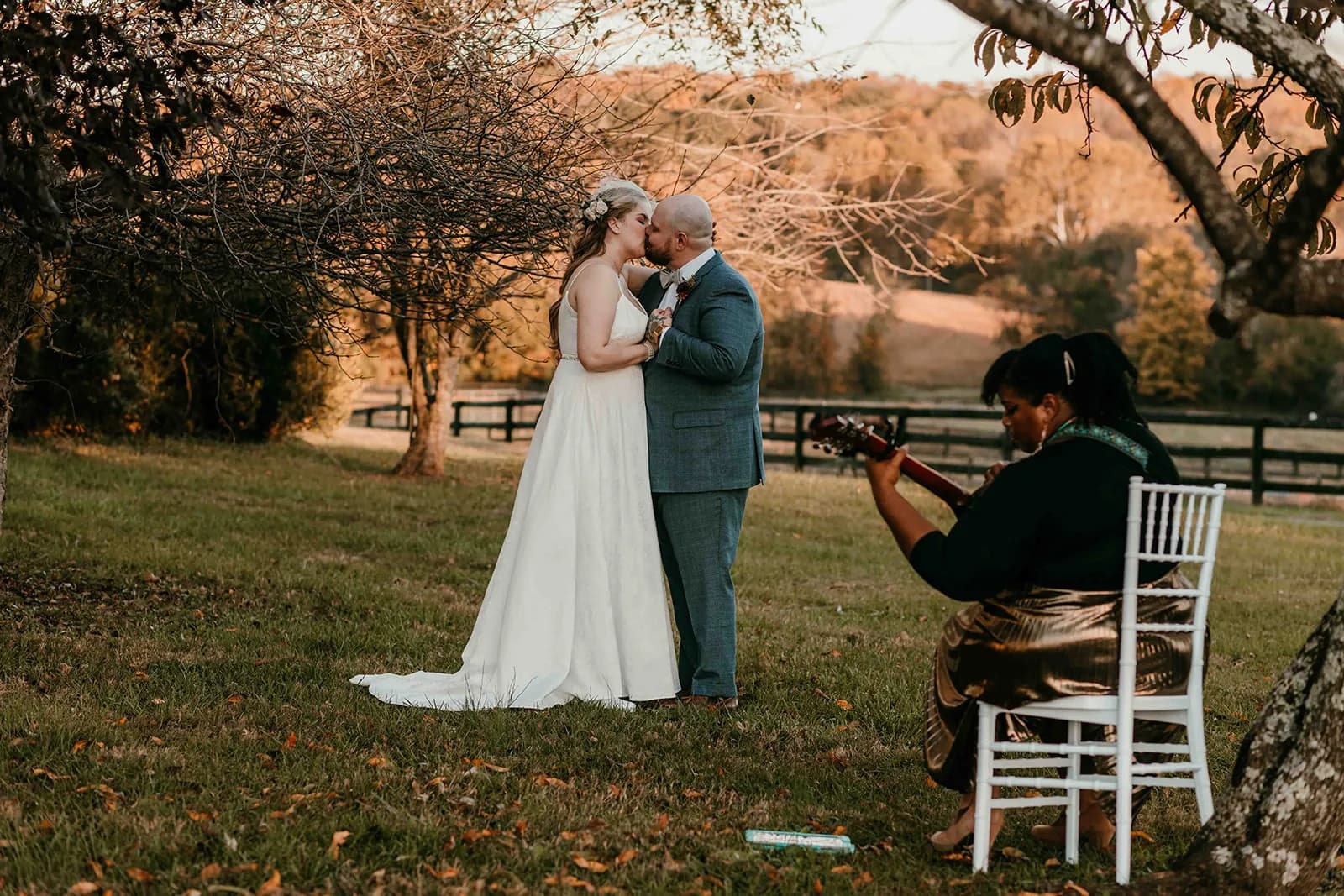 Bride and groom share first kiss on Rixey Manor grounds at golden hour while guitarist plays nearby