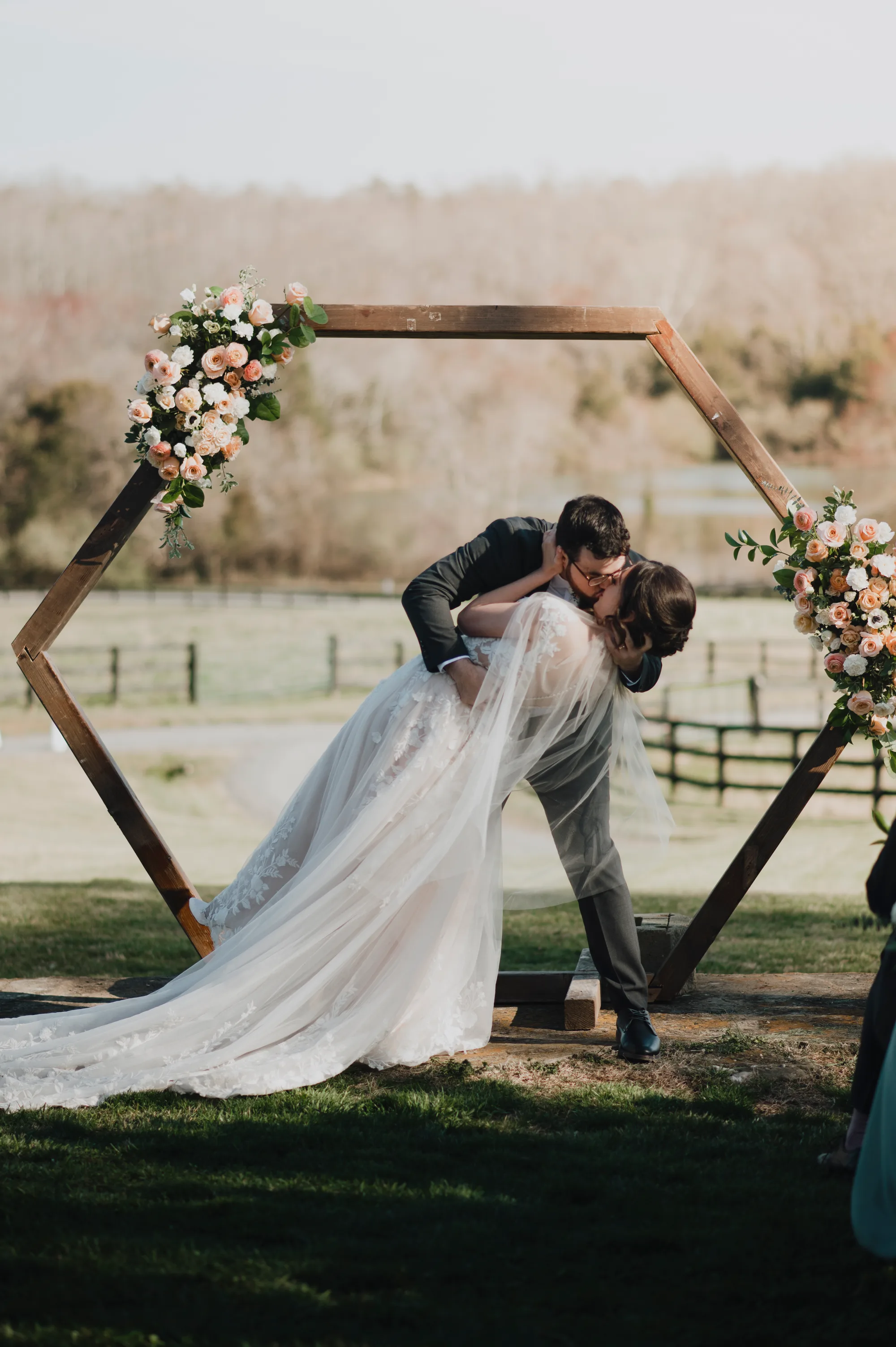 Groom dips bride for first kiss under hexagonal floral arch at Rixey Manor outdoor ceremony with pastoral Virginia backdrop
