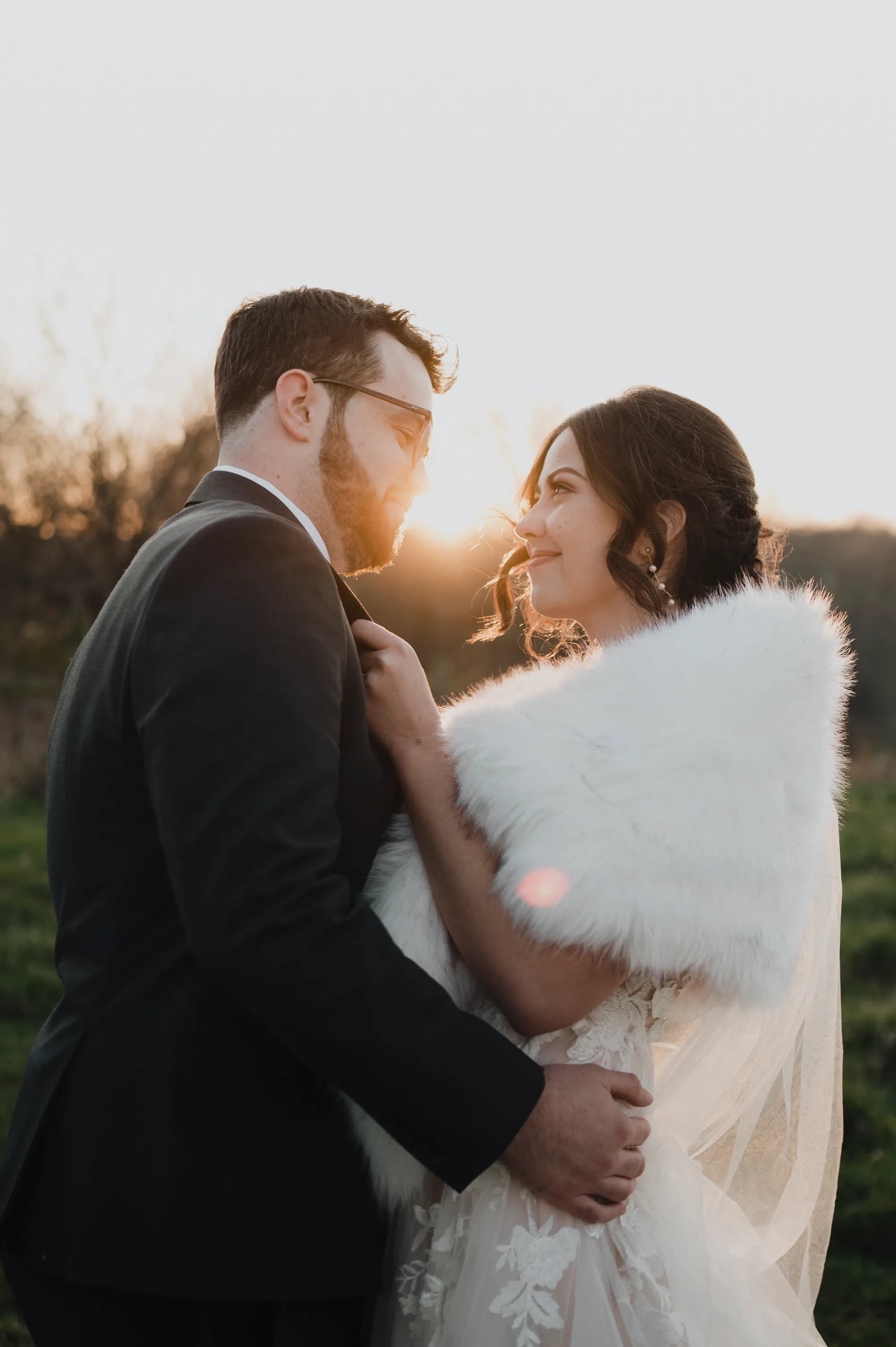 Bride in fur stole gazes at groom during golden hour portrait on Rixey Manor grounds