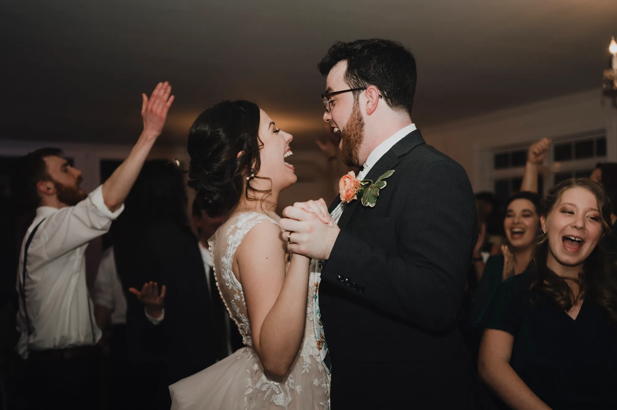 Bride and groom laugh together on the dance floor surrounded by cheering guests at their wedding reception