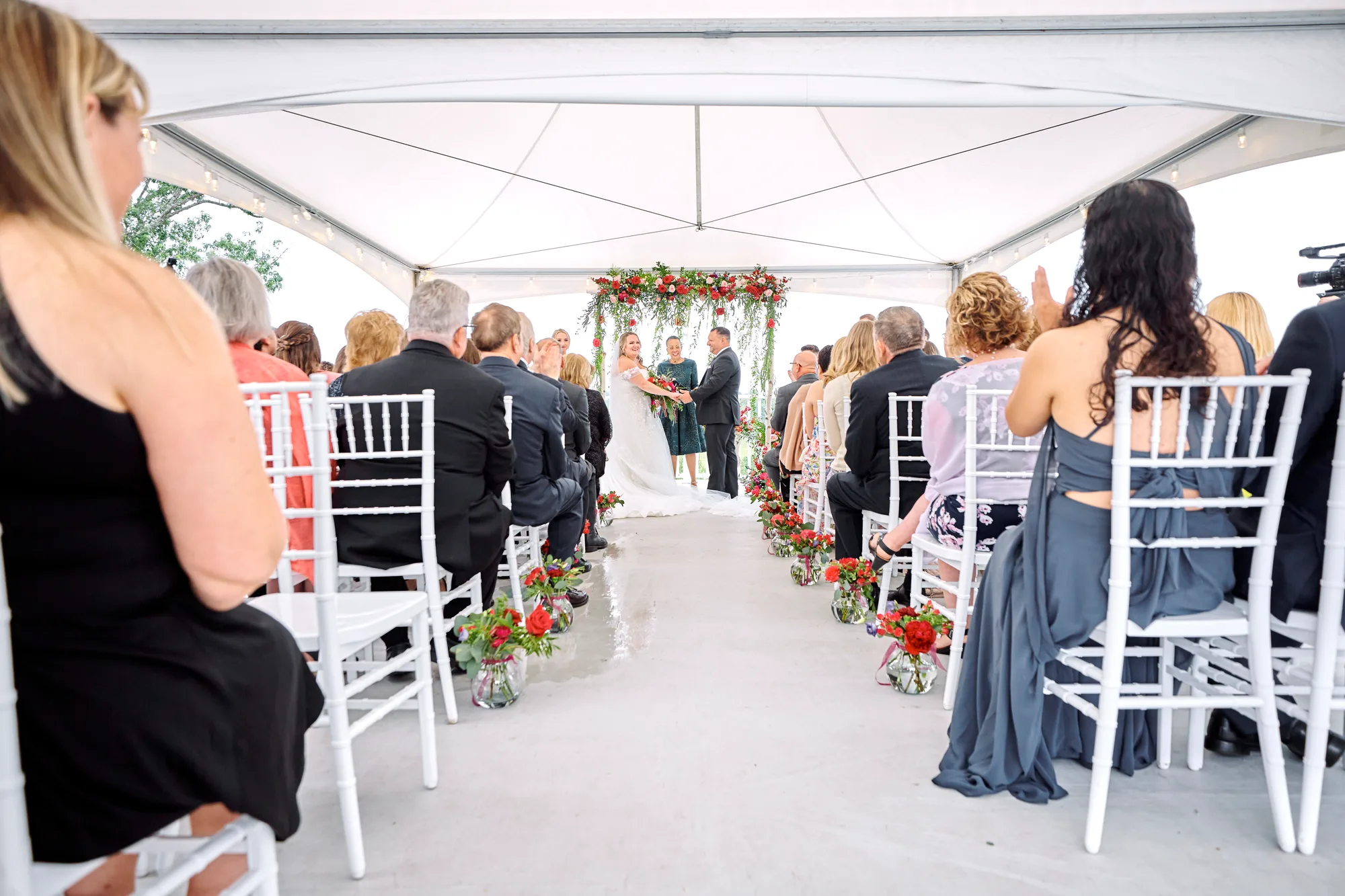 Wide aisle view of outdoor tent ceremony with floral arch and guests seated on white chairs at Rixey Manor