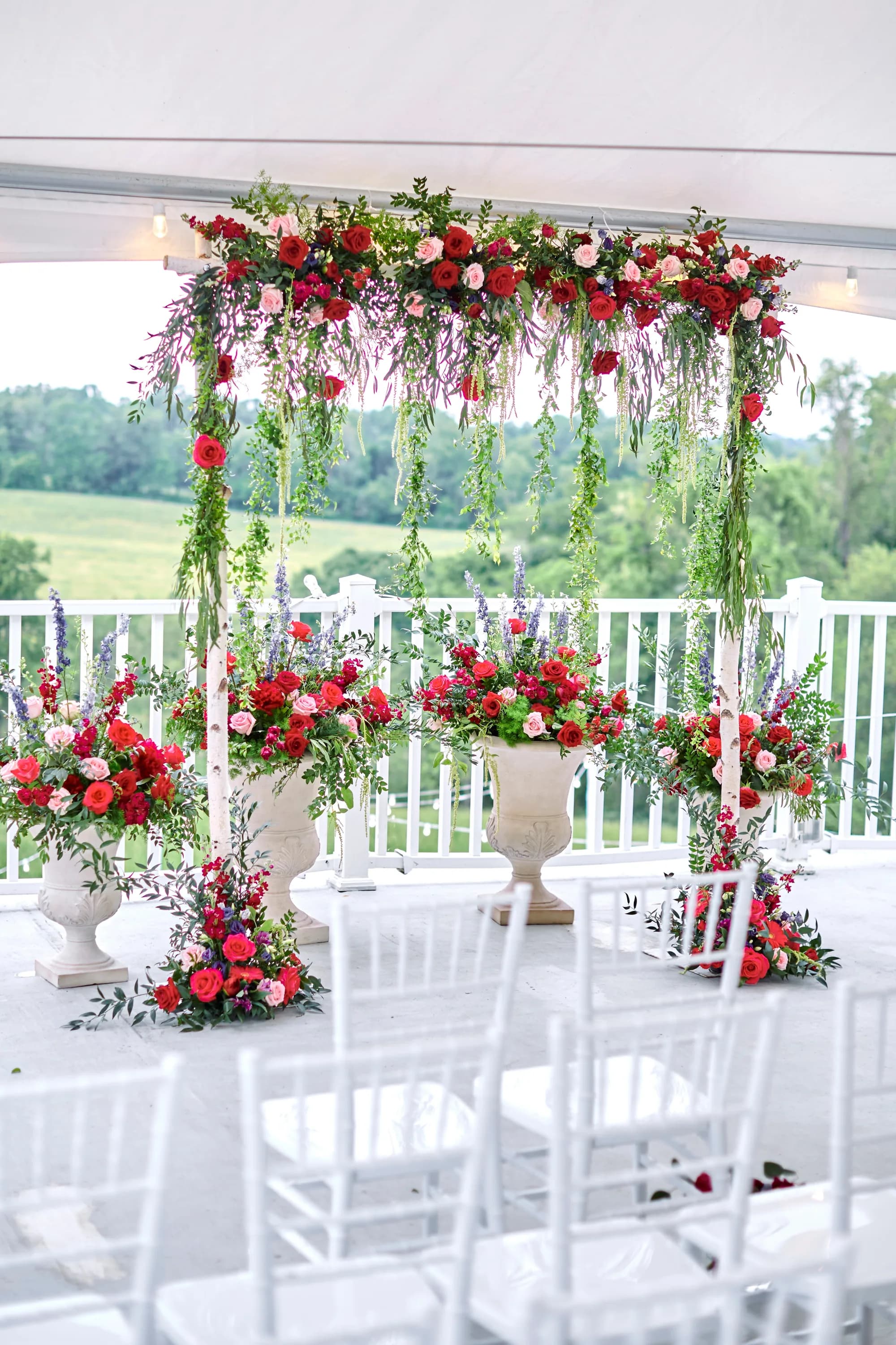 Lush floral arch with red roses and greenery at Rixey Manor terrace ceremony site overlooking rolling Virginia hills