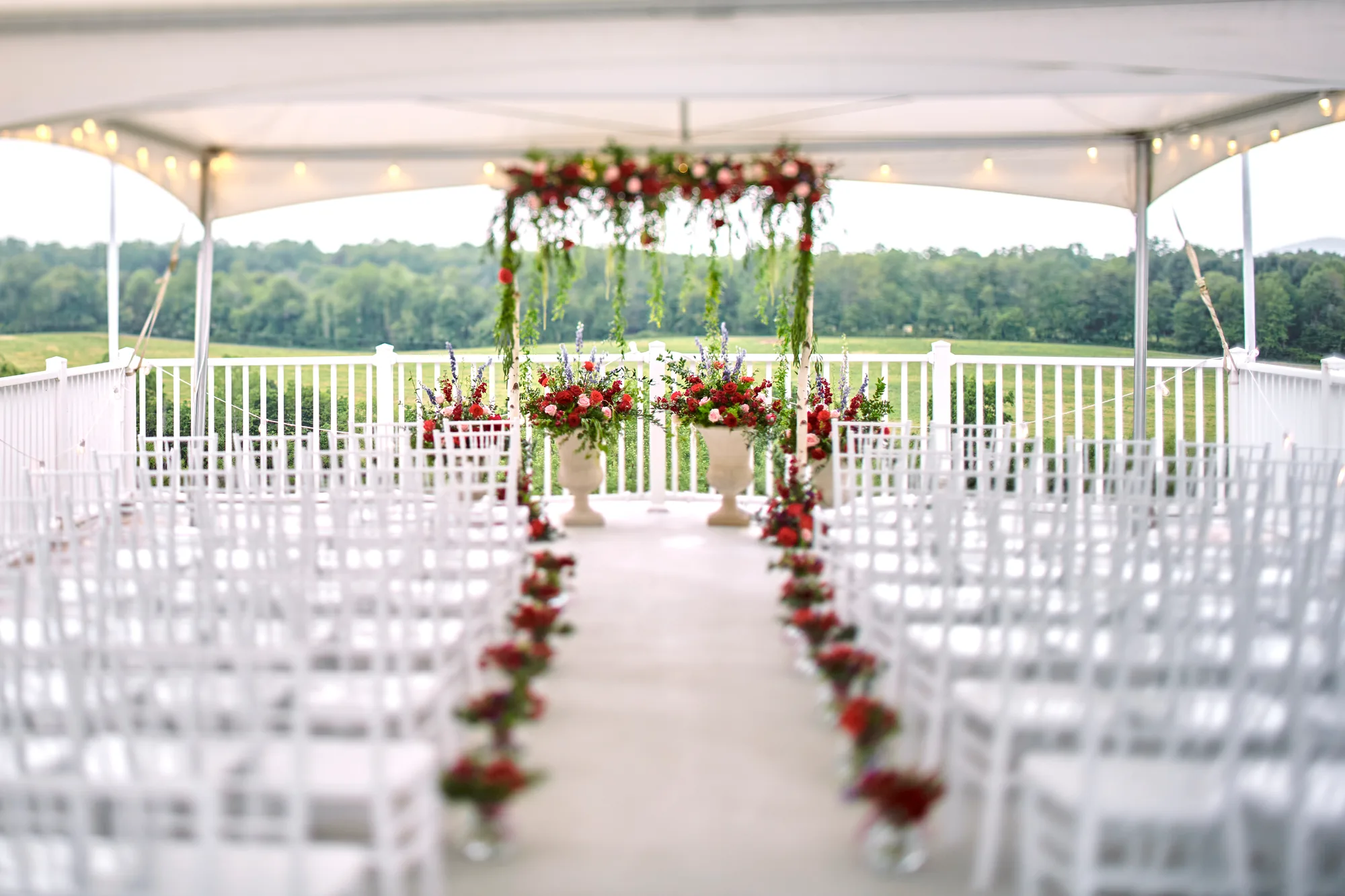 Floral arch and red rose-lined aisle set for a wedding ceremony on Rixey Manor's scenic outdoor terrace