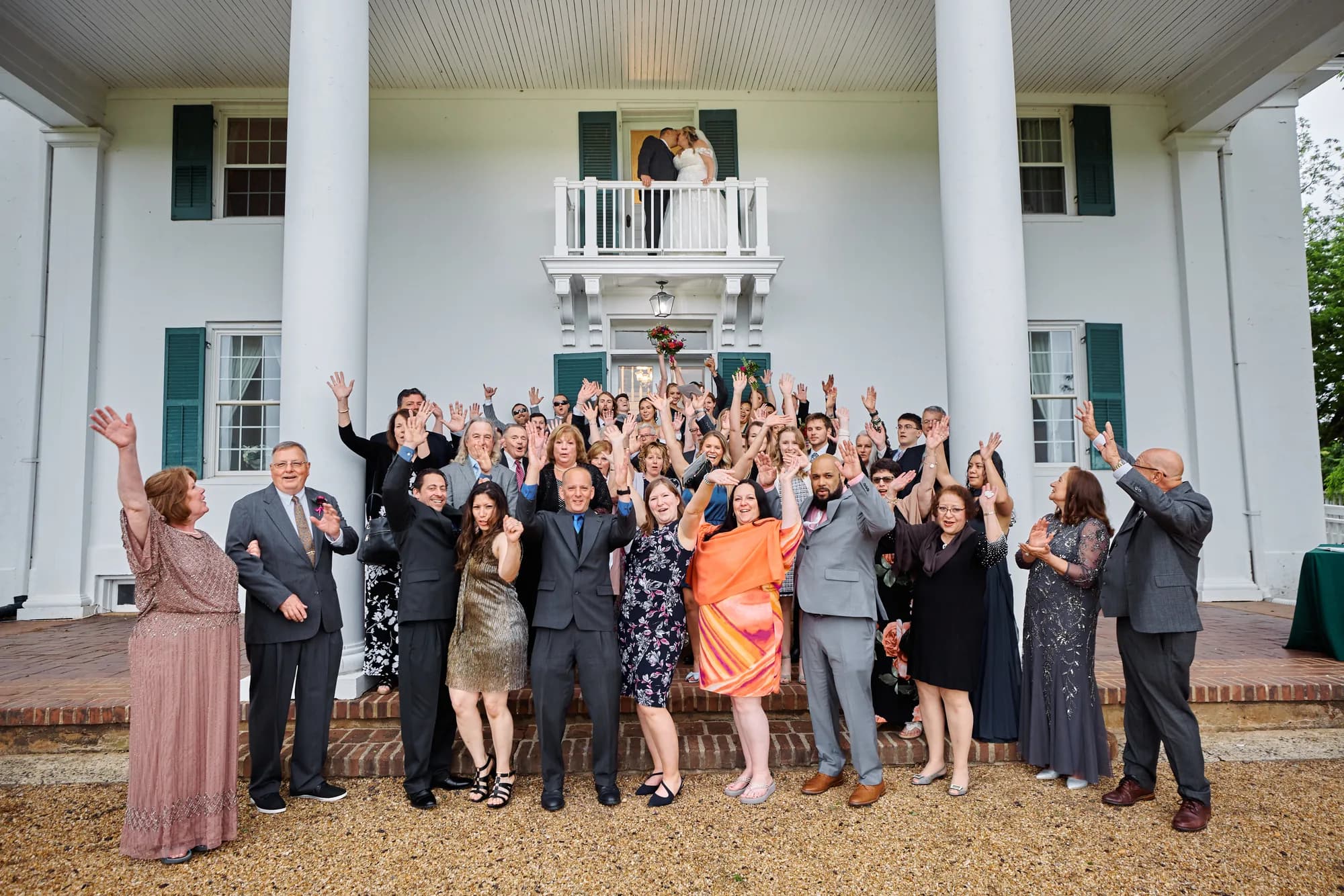 Wedding guests cheer as couple kisses on Rixey Manor's white-columned balcony in Virginia