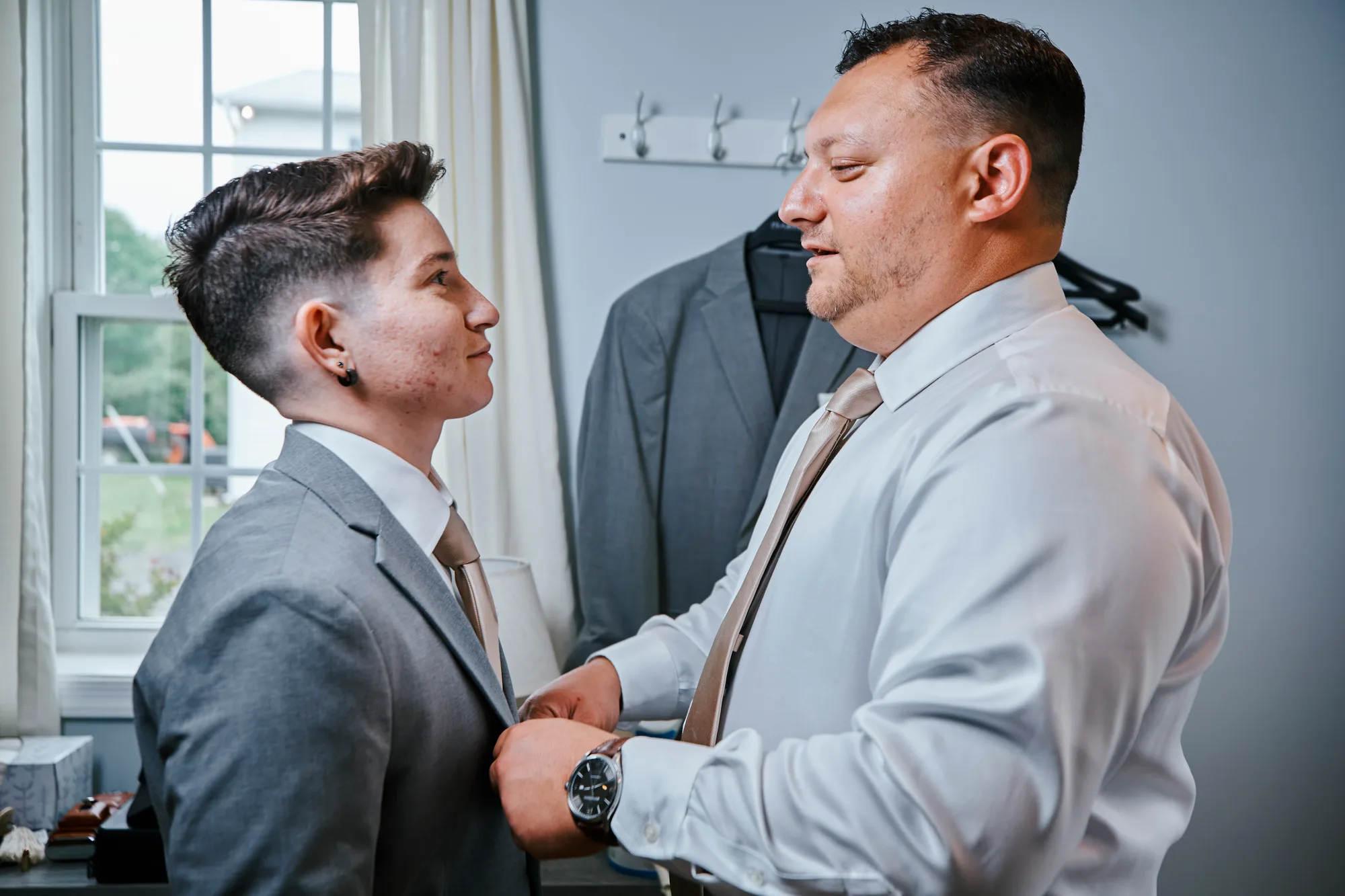 Two partners help each other with ties while getting ready, sharing a warm smile before the ceremony