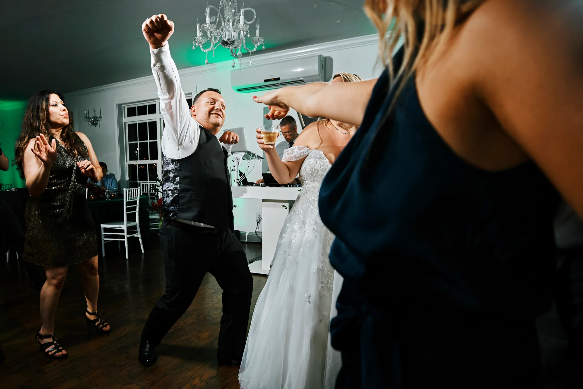 Groom dancing joyfully with raised fist beside bride and guests on the reception dance floor