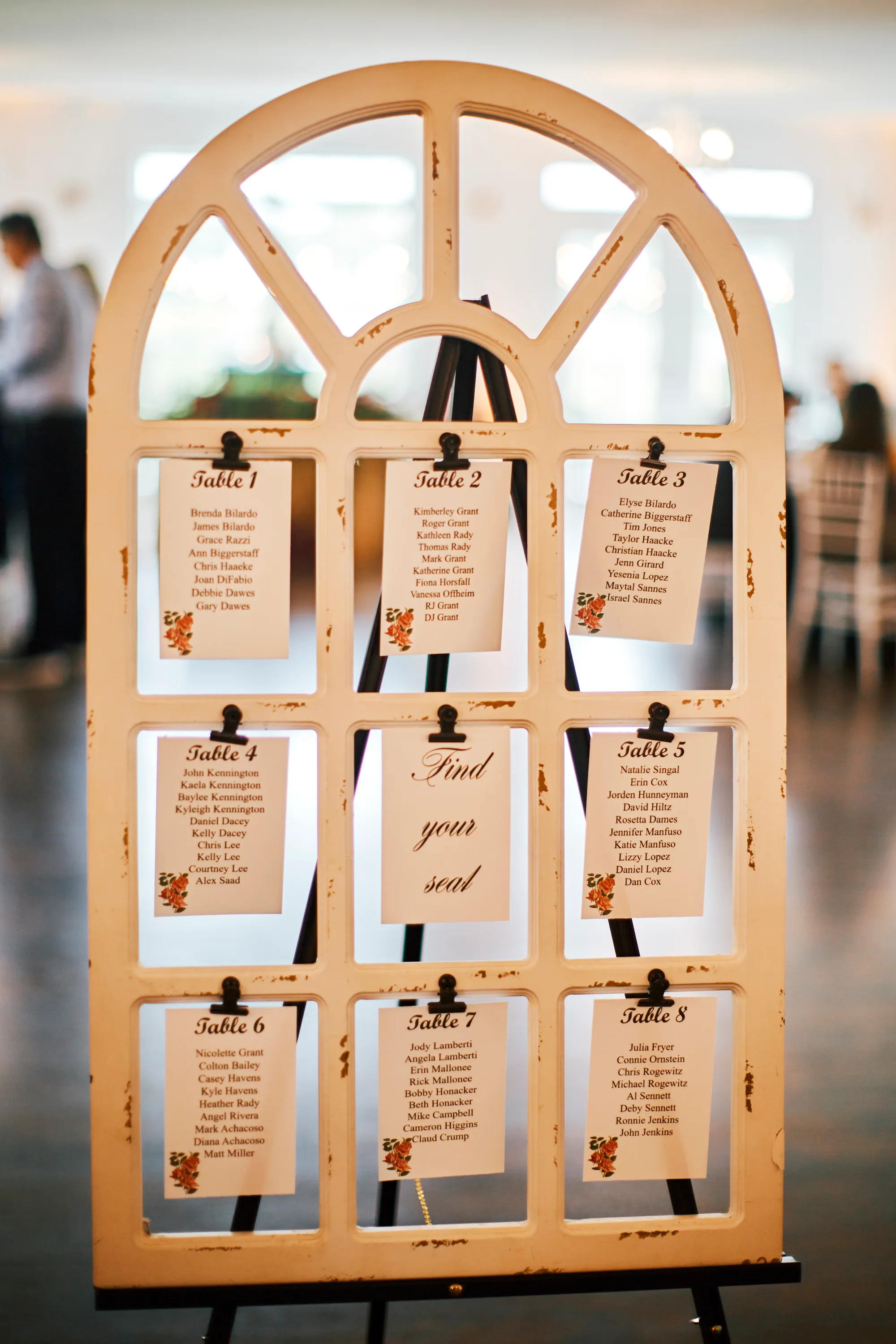 Elegant wedding seating chart displayed on a vintage arched window frame on a black easel
