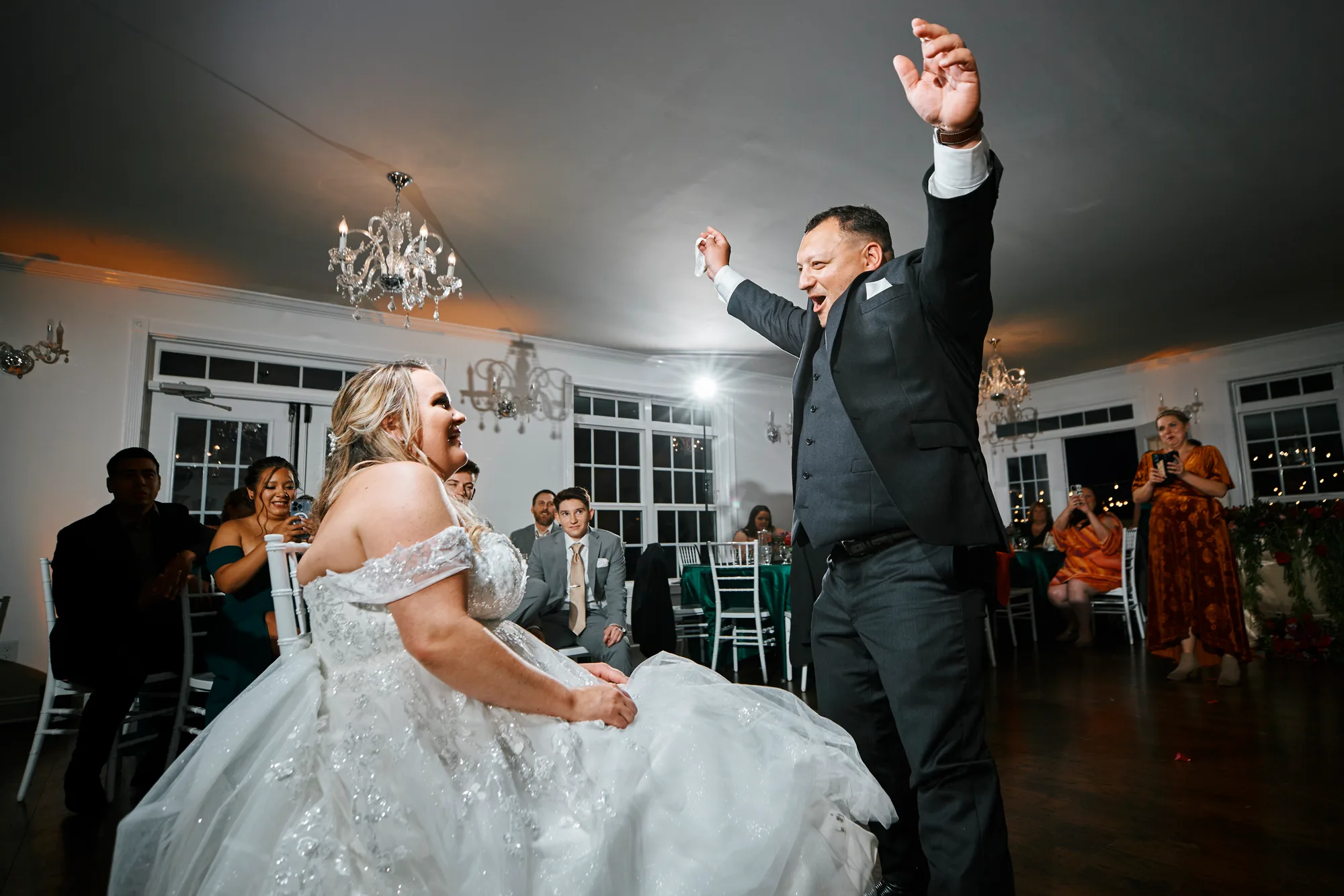 Bride and groom dancing energetically under chandeliers at Rixey Manor reception as guests cheer