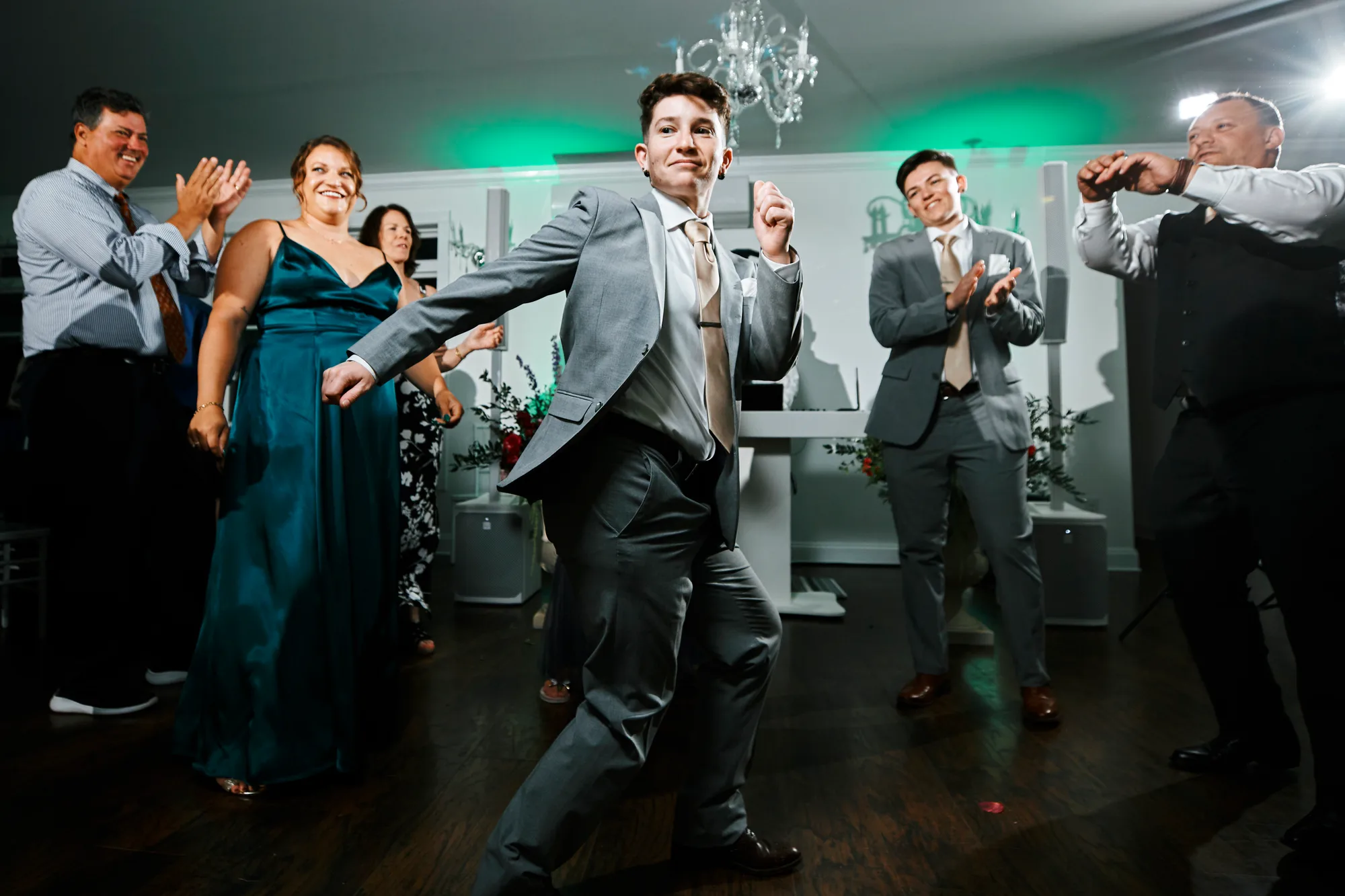 Groom busts a move on the dance floor as wedding guests cheer and clap at reception