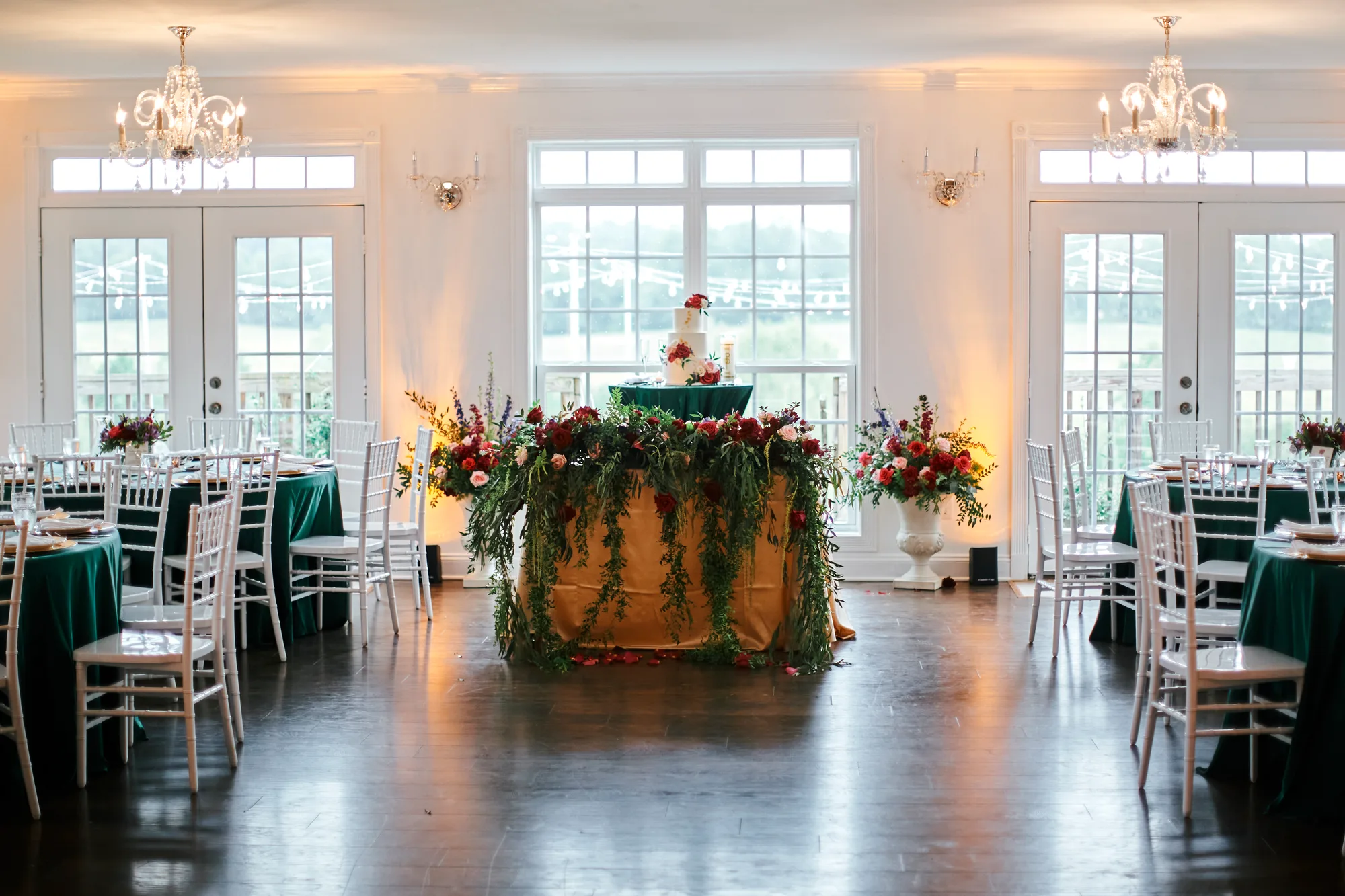 Elegant Rixey Manor ballroom with emerald linens, floral cake table, chandeliers, and French doors overlooking Virginia countryside