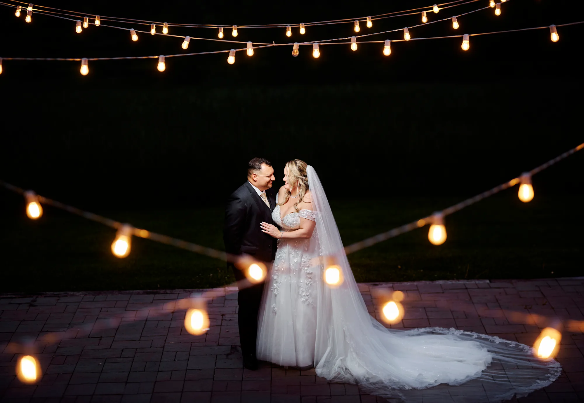 Bride and groom dancing under string lights at night during evening portrait session