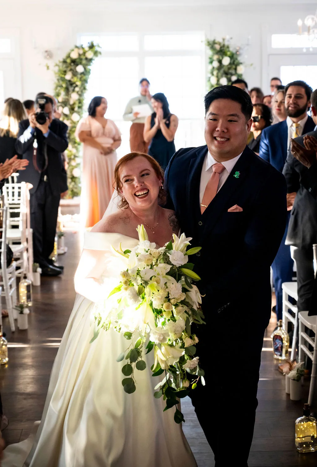 Joyful newlyweds walk back down the aisle at Rixey Manor ceremony room, guests applauding, bride laughing with cascading bouquet