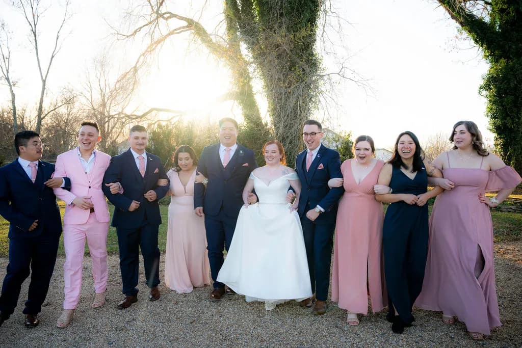 Joyful wedding party in pink and navy laughing together outdoors at golden hour