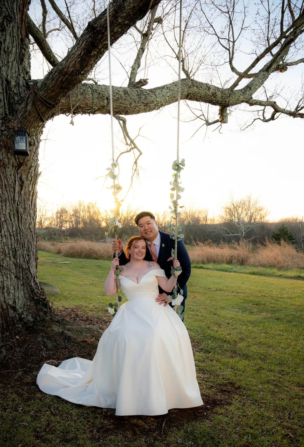 Bride and groom smile on a floral rope swing beneath a large tree at golden hour on Rixey Manor grounds.