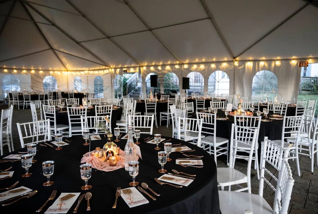 Elegant black-linened reception tables with gold accents under string lights in Rixey Manor's tent venue
