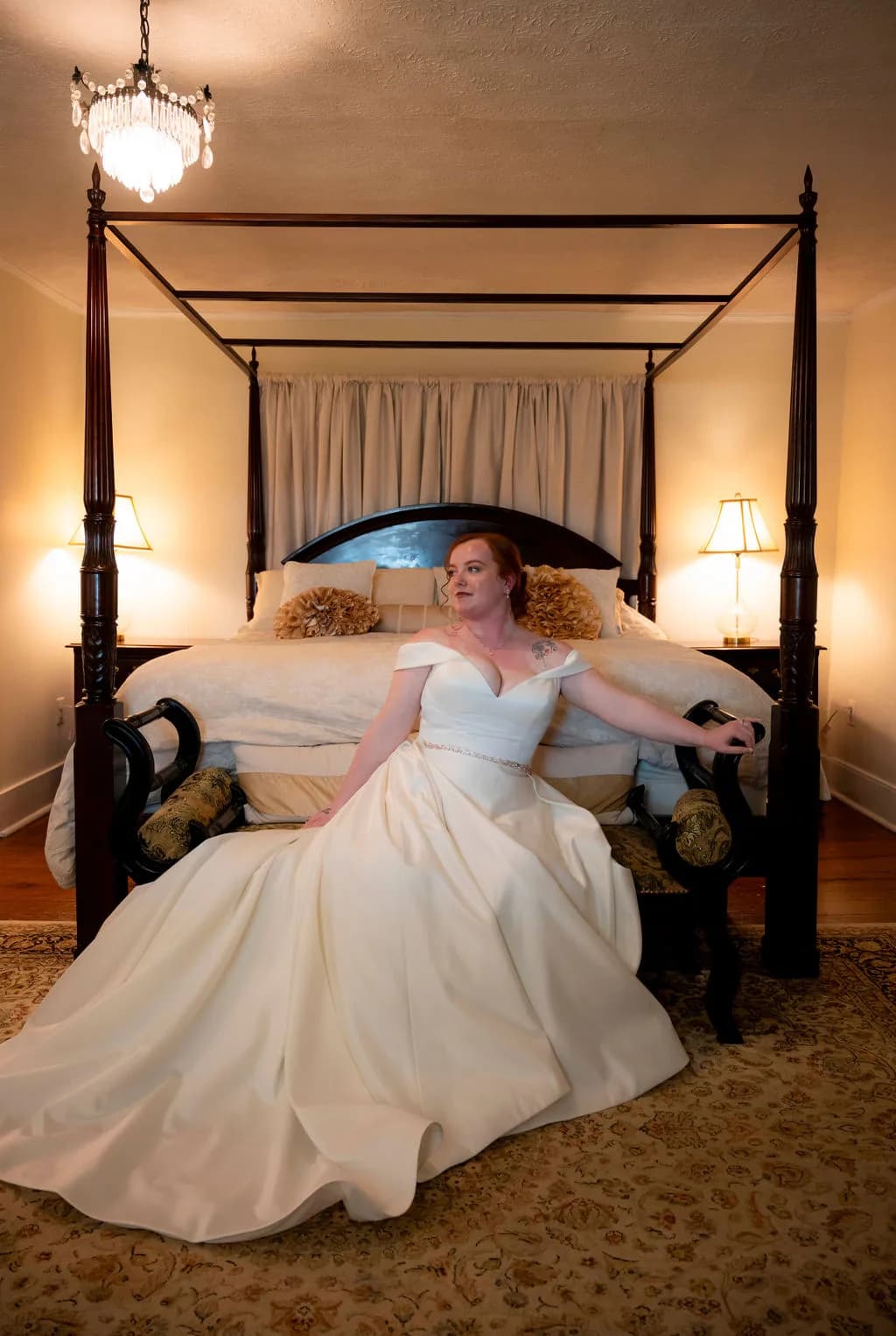 Bride in white gown posing on four-poster canopy bed in elegant bedroom with warm lighting