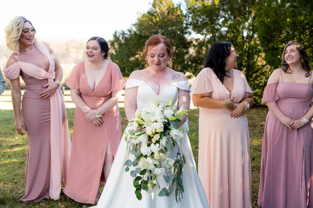Bride holding white bouquet laughs with four bridesmaids in pink dresses on Rixey Manor grounds