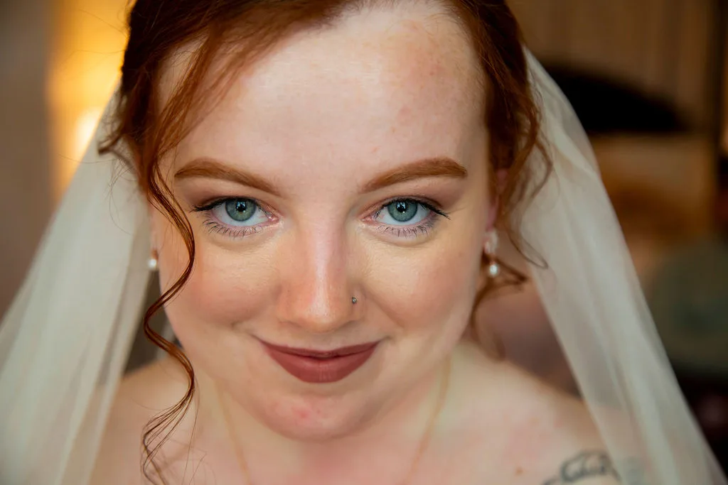 Close-up portrait of a smiling red-haired bride in veil with blue eyes and subtle wedding makeup