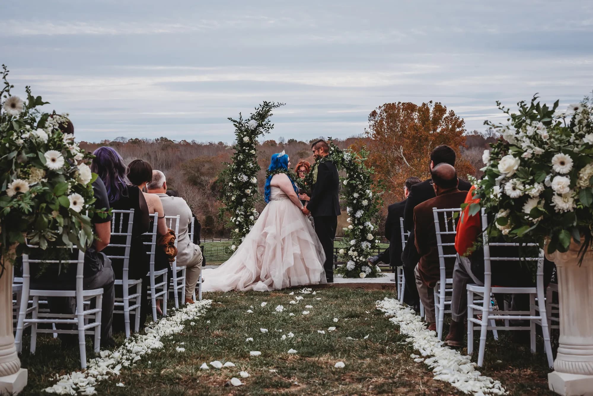 Couple exchanges vows under floral arch at Rixey Manor outdoor ceremony, guests seated along petal-lined aisle