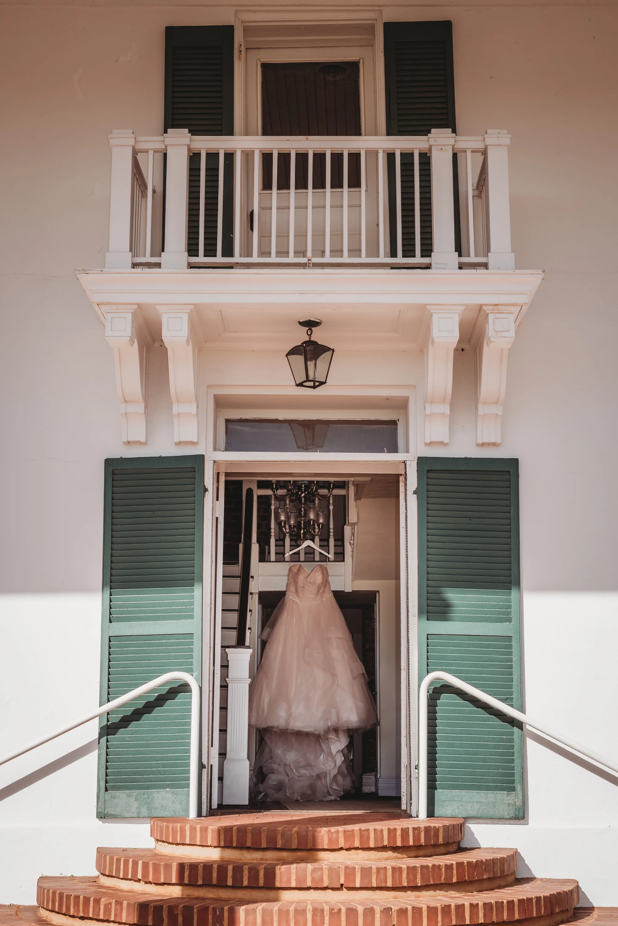 Wedding gown hanging in the doorway of Rixey Manor's historic facade with green shutters and brick steps