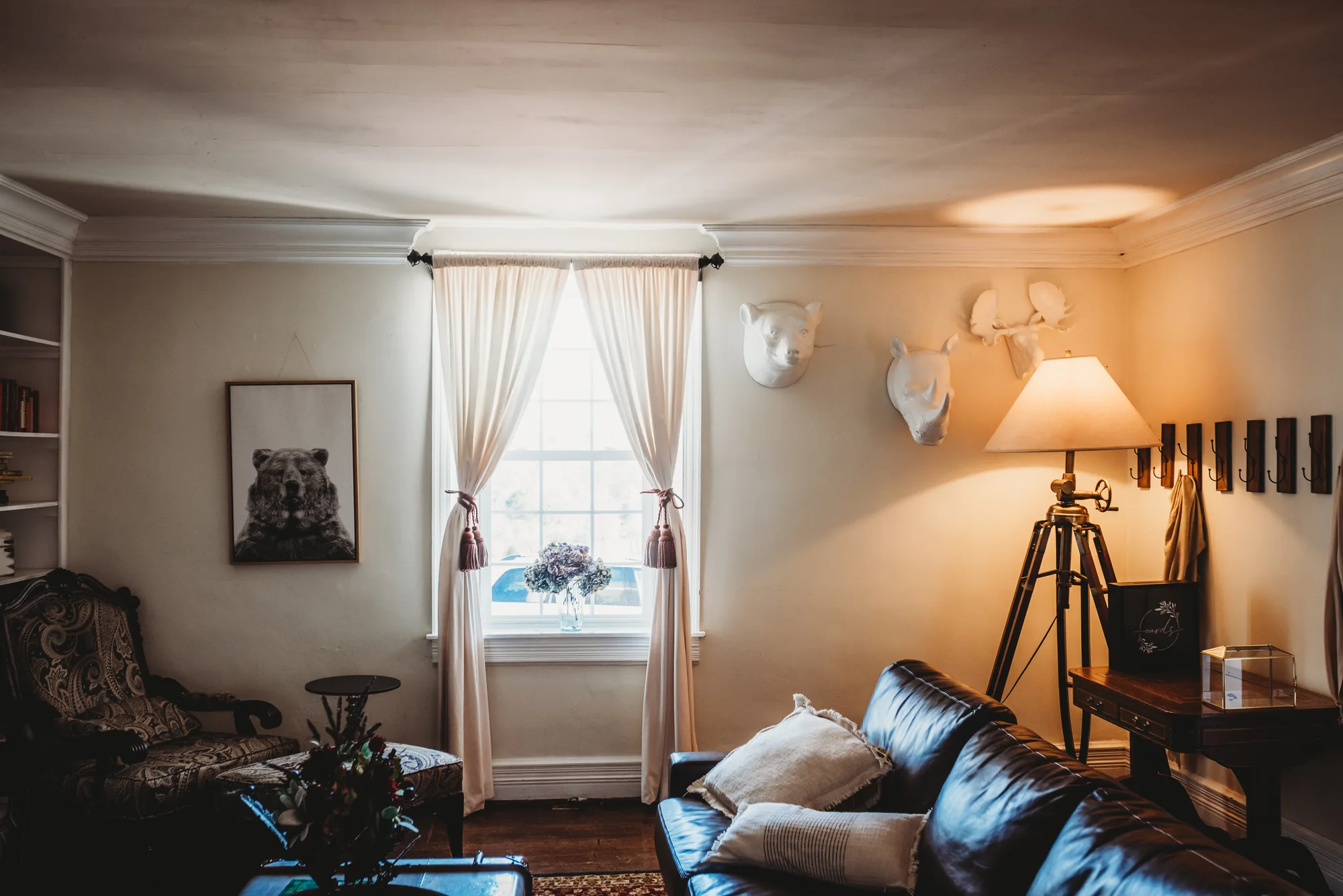 Cozy sitting room at Rixey Manor with leather sofa, sheer curtains, and mounted animal heads on warm-lit walls.