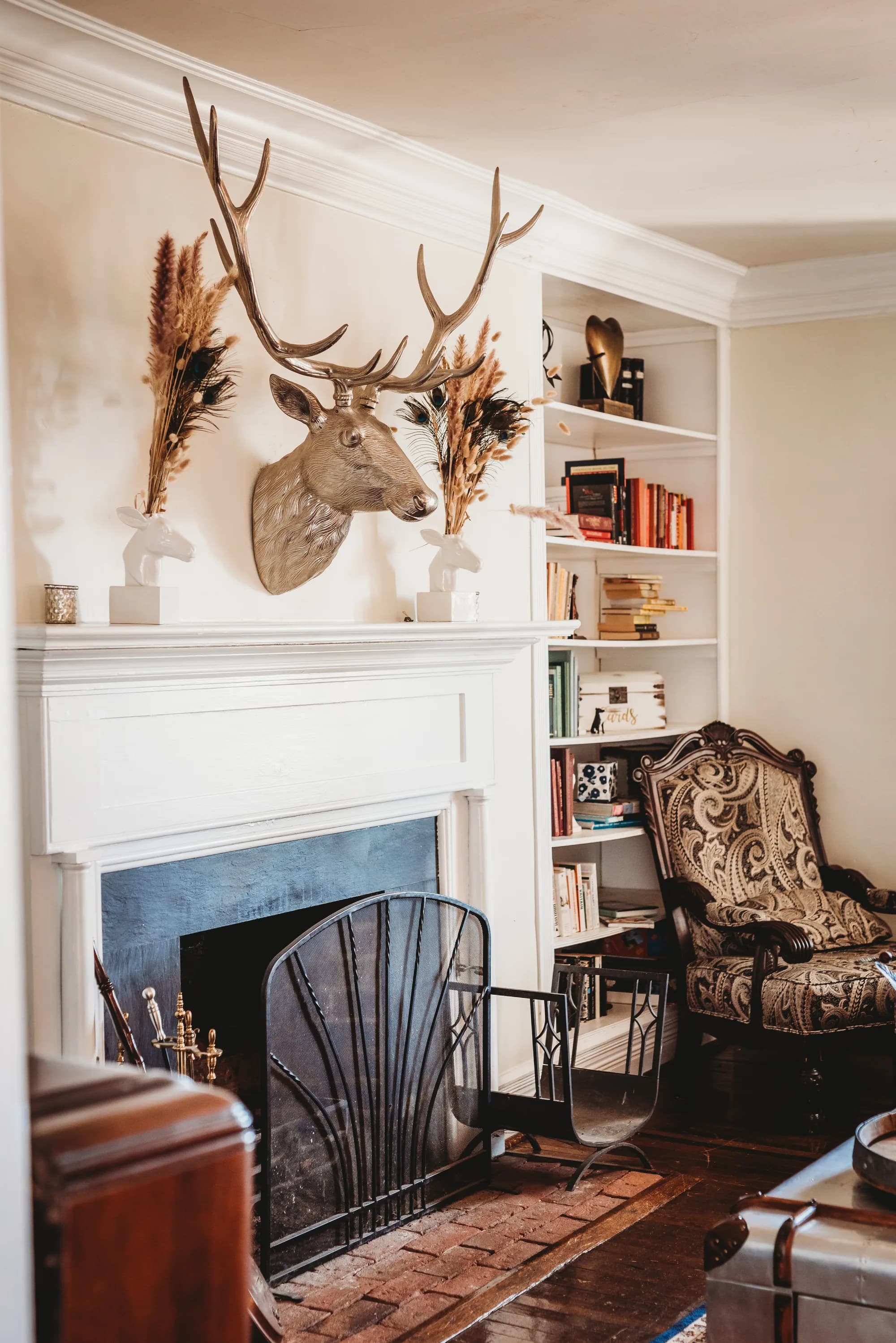 Cozy Rixey Manor sitting room with white fireplace, decorative stag mount, built-in bookshelves, and ornate armchair