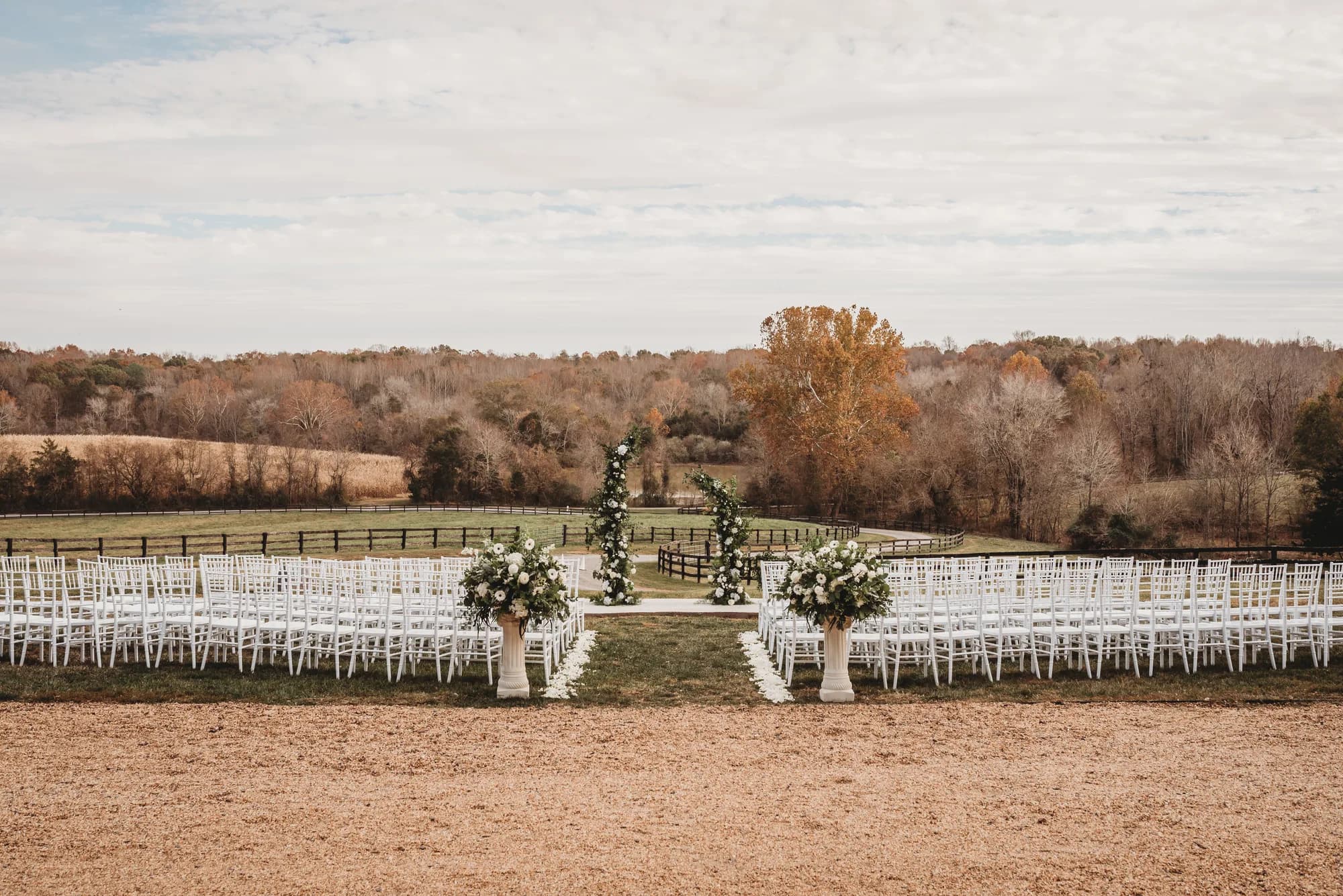 Outdoor ceremony setup with white chairs, floral arch, and rolling Virginia countryside in autumn