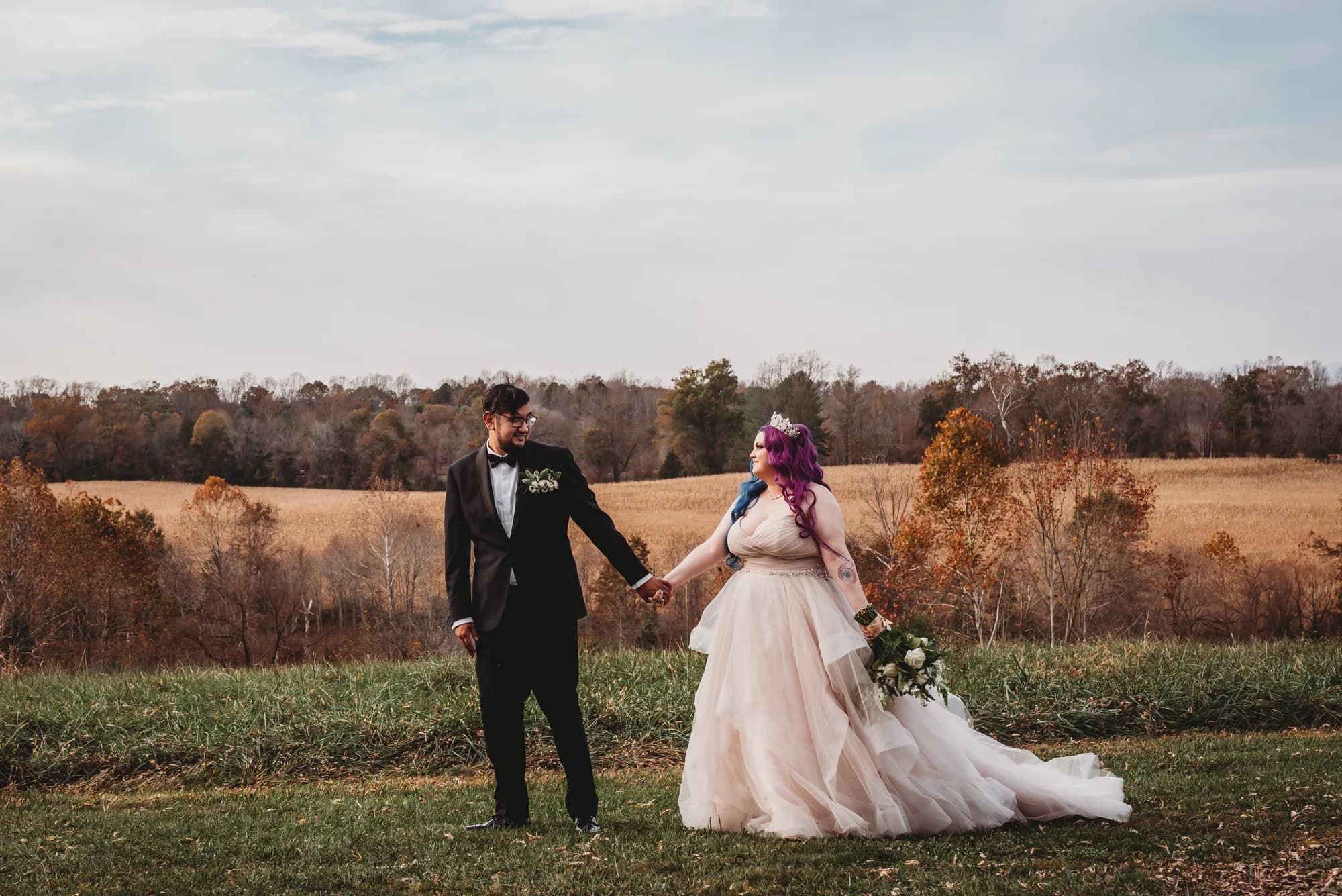 Bride and groom holding hands on Rixey Manor's autumn hillside, overlooking golden fields and tree line