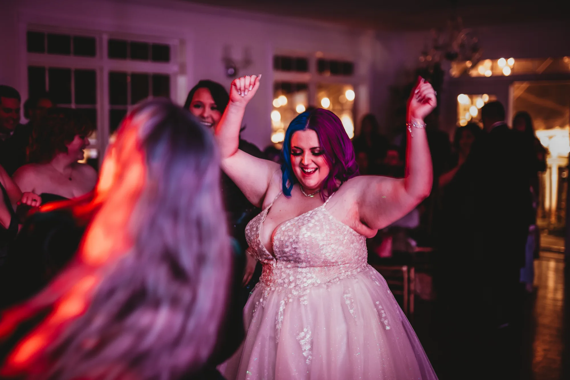 Bride with blue and purple hair dances joyfully with arms raised at Rixey Manor wedding reception