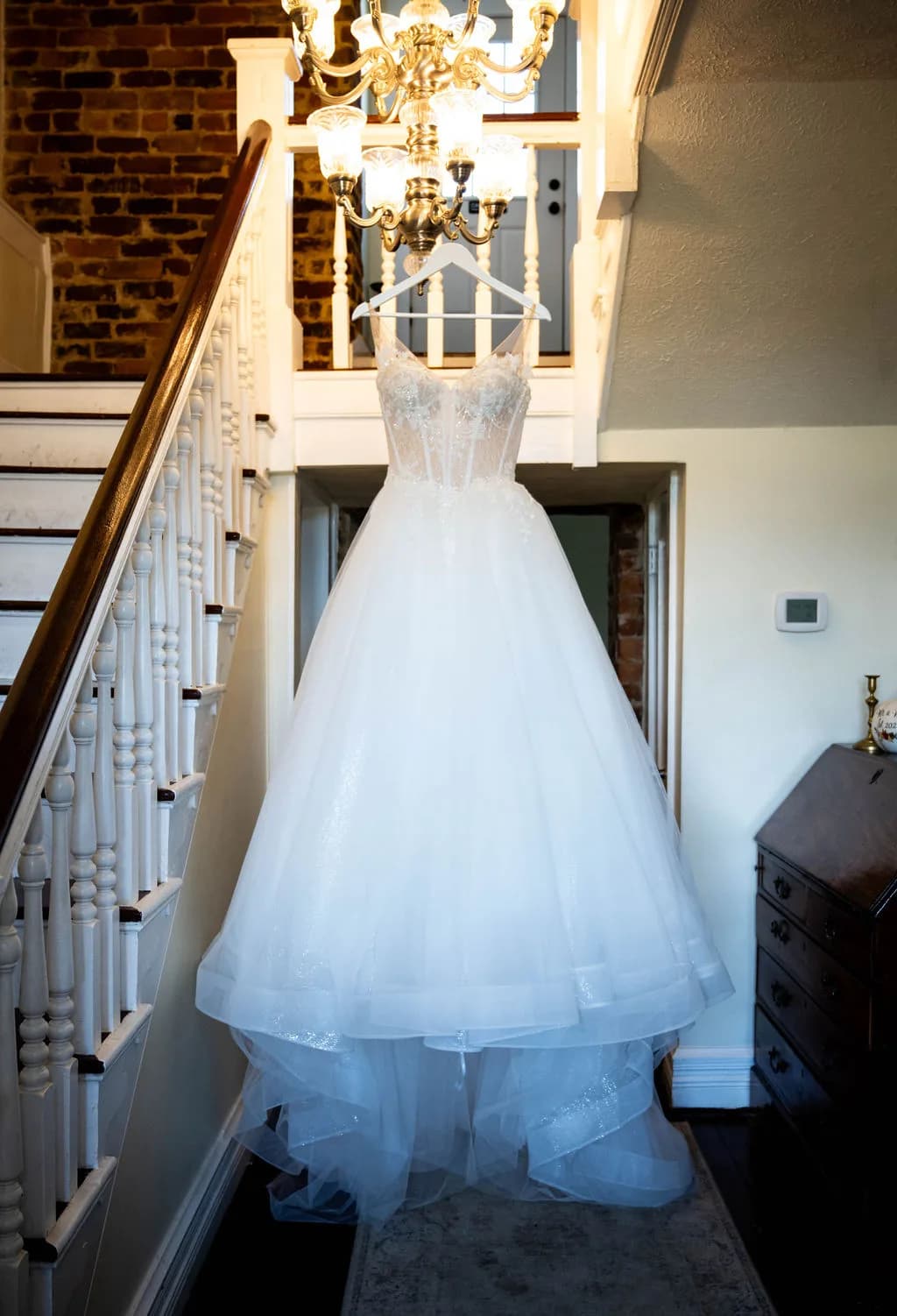 White ball gown wedding dress hanging from chandelier above staircase at Rixey Manor
