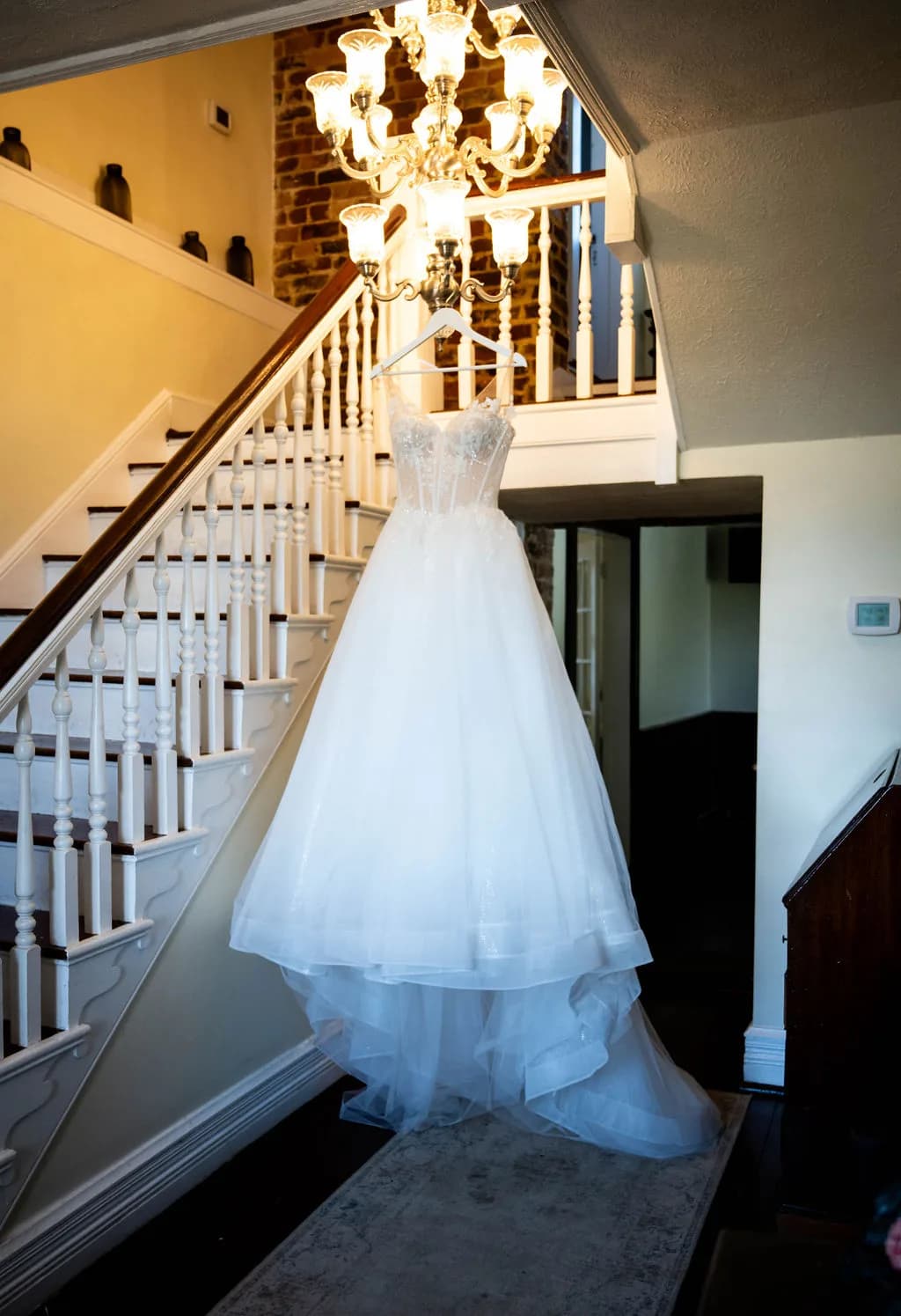 White wedding dress on mannequin displayed in manor hallway with staircase and chandelier