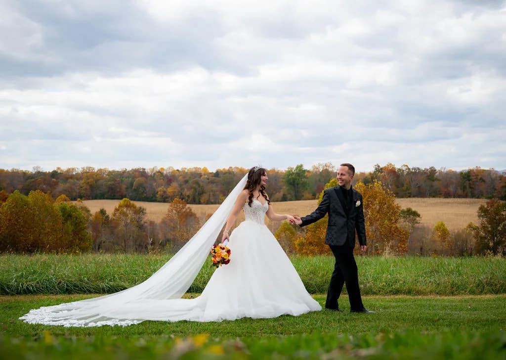 Bride and groom walk hand-in-hand across Rixey Manor's hillside lawn amid vibrant autumn foliage