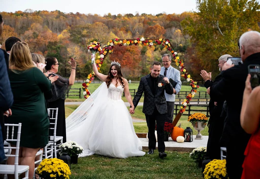 Bride and groom exit ceremony under floral arch at Rixey Manor, surrounded by vibrant fall foliage and cheering guests.