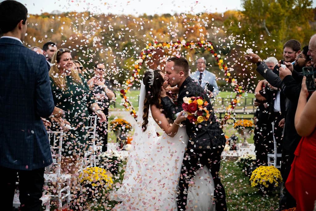 Bride and groom kiss as guests shower them with confetti during fall outdoor ceremony at Rixey Manor