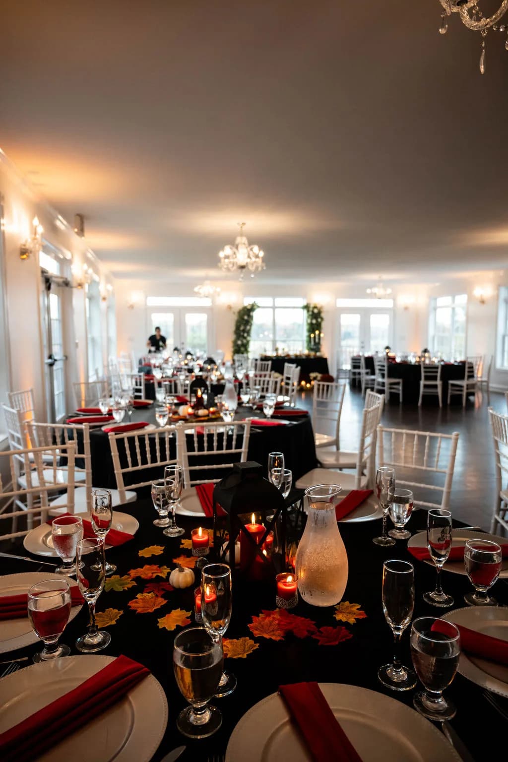 Fall-themed reception tables with black linens, red napkins, autumn leaves, and candlelit lanterns in the Rixey Manor ballroom