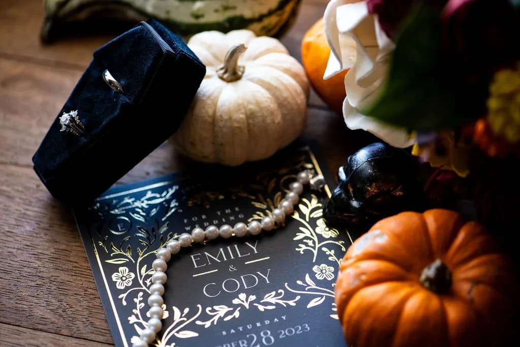 Wedding detail shot with white and orange pumpkins, black coffin box, and personalized program on wooden surface
