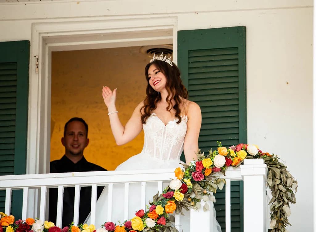 Smiling bride in tiara waves from flower-adorned balcony at Rixey Manor historic estate