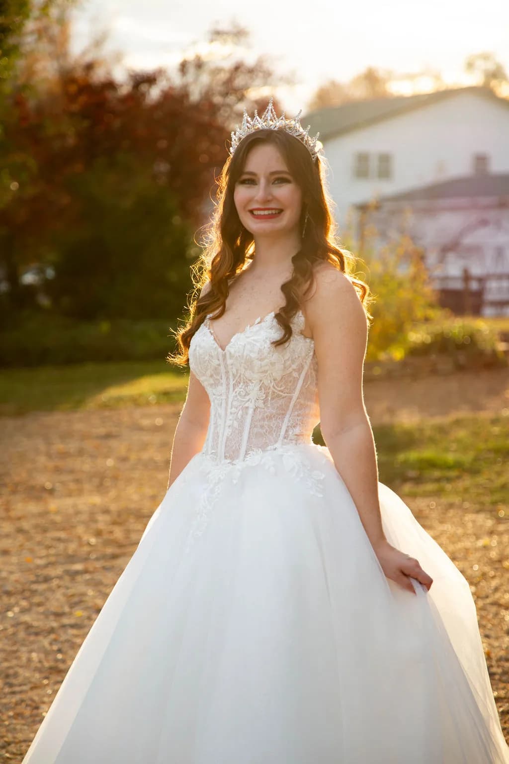 Radiant bride in lace corset gown and crystal crown smiling in golden hour light on estate grounds