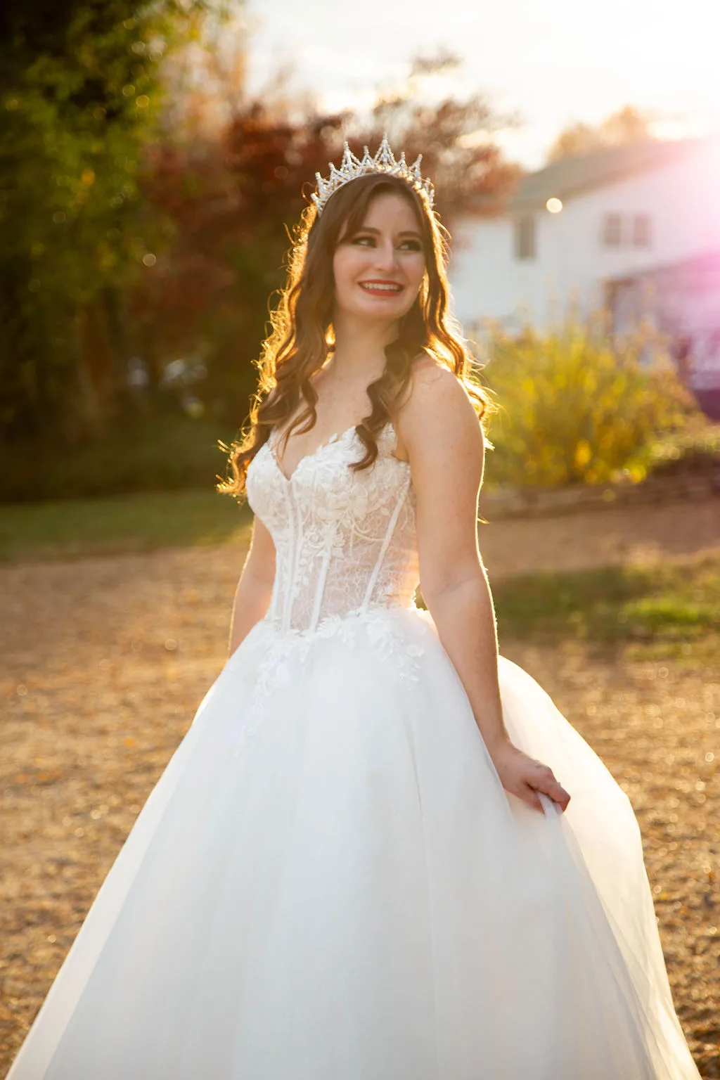 Radiant bride in lace ballgown and crystal tiara smiling during golden hour portrait session outdoors